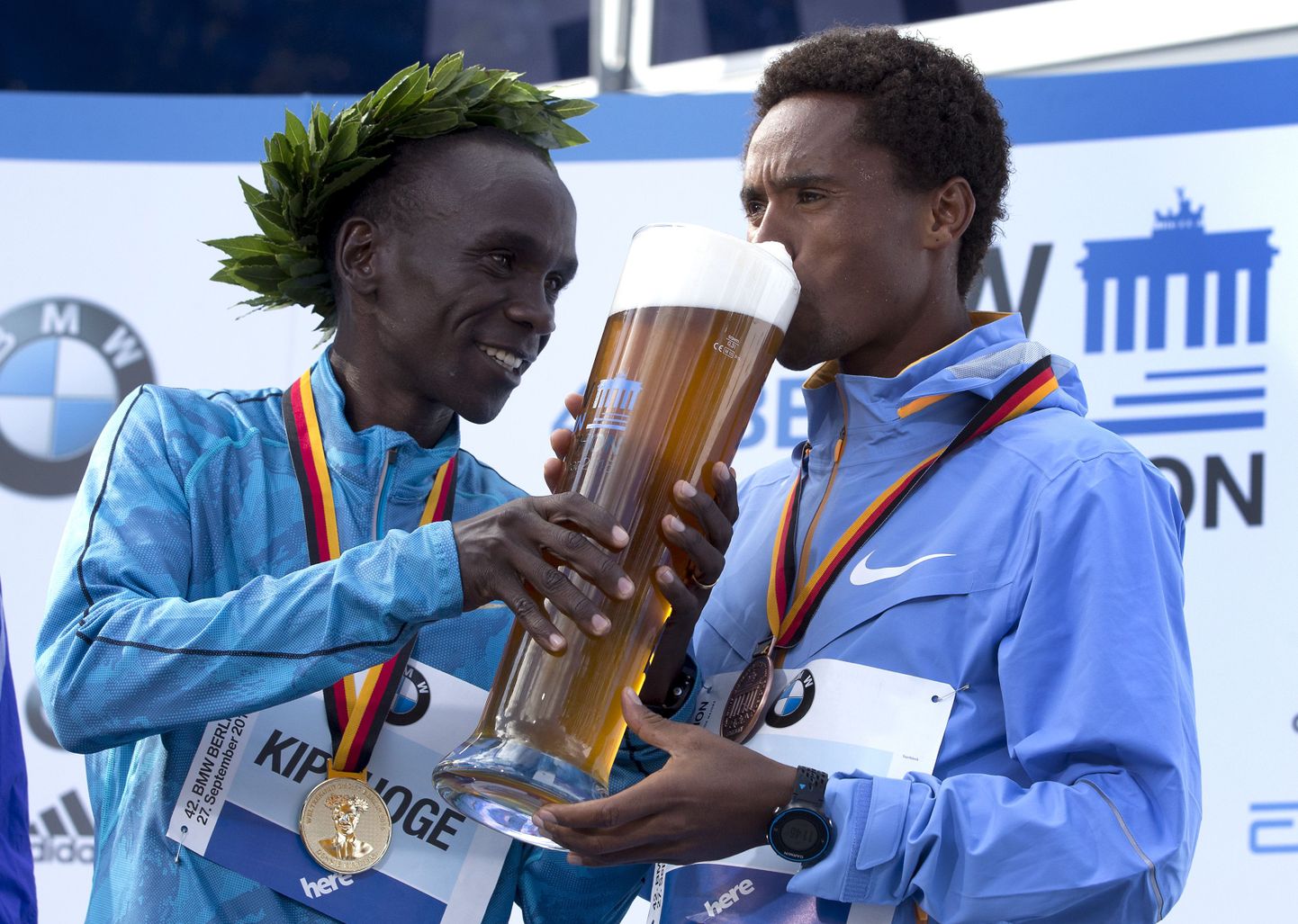 Berliini maratoni võitja Eliud Kipchoge (vasakul) aitab kolmanda koha mehel Feyisa Lilesal kummutada traditsioonilist õlleklaasi.