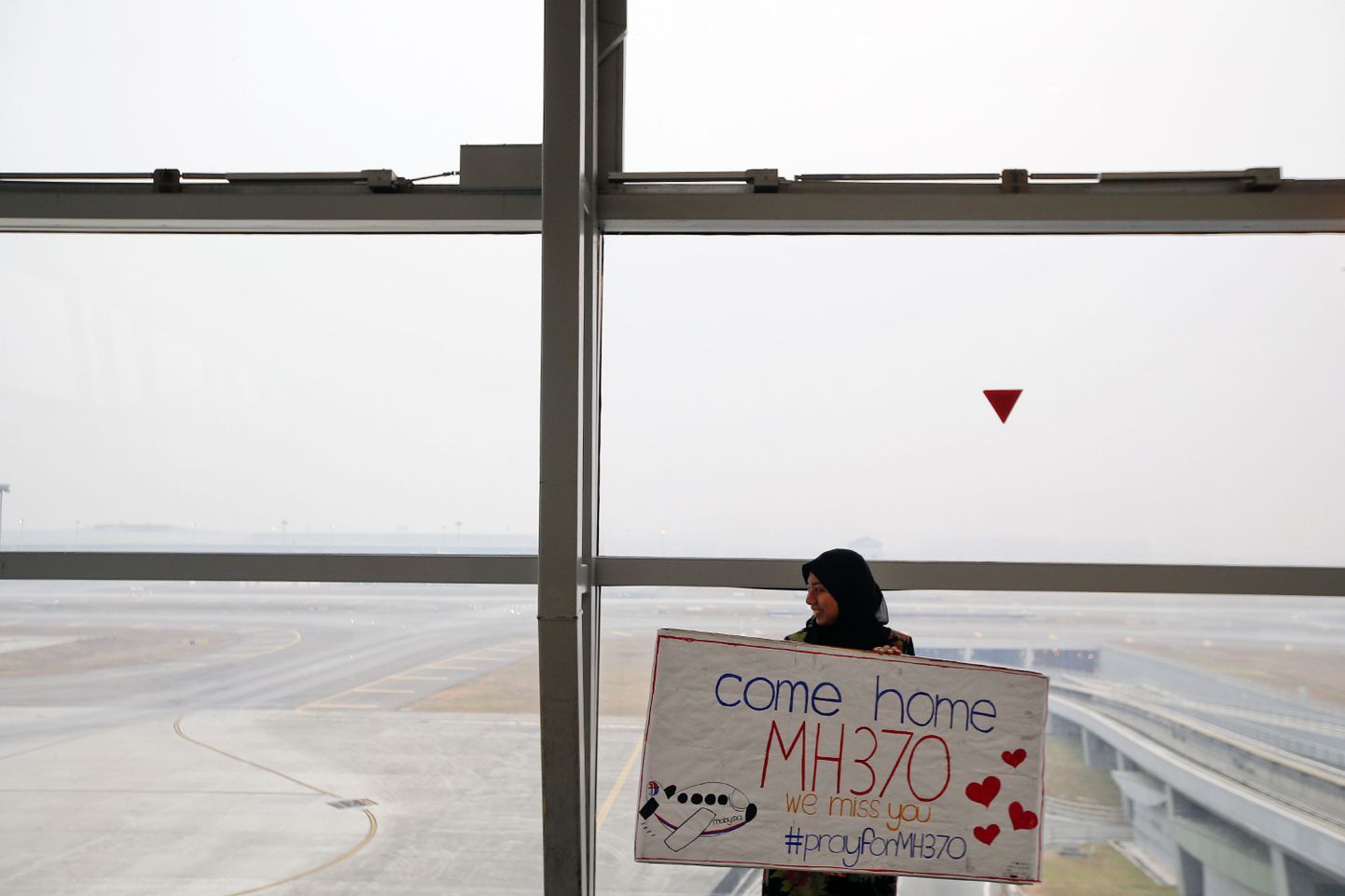 Kuala Lumpuri lennujaamas olev naine hoiab käes plakatit, millel oleva kirja põhjal oodatakse kadunud lennukit koju.