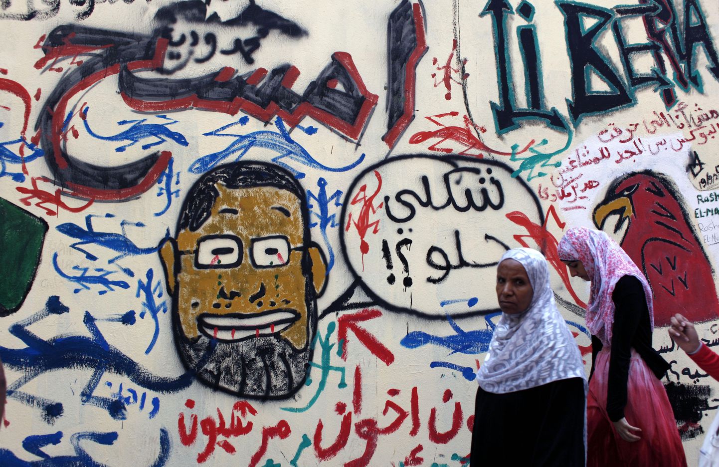 Naised seina ääres, kuhu on joonistatud Egiptuse presidenti Mohamed Morsit kujutav karikatuur.