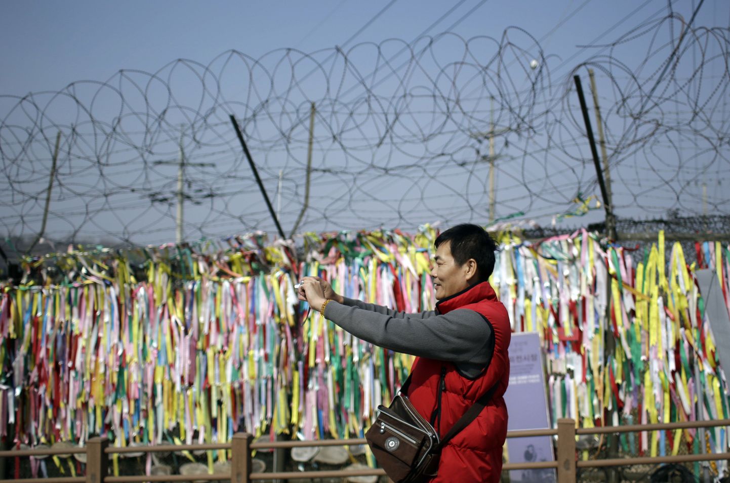 Mees pildistab okastraataial olevaid lindikesi, mille sõnumiks on soov kahe Korea ühinemisest.