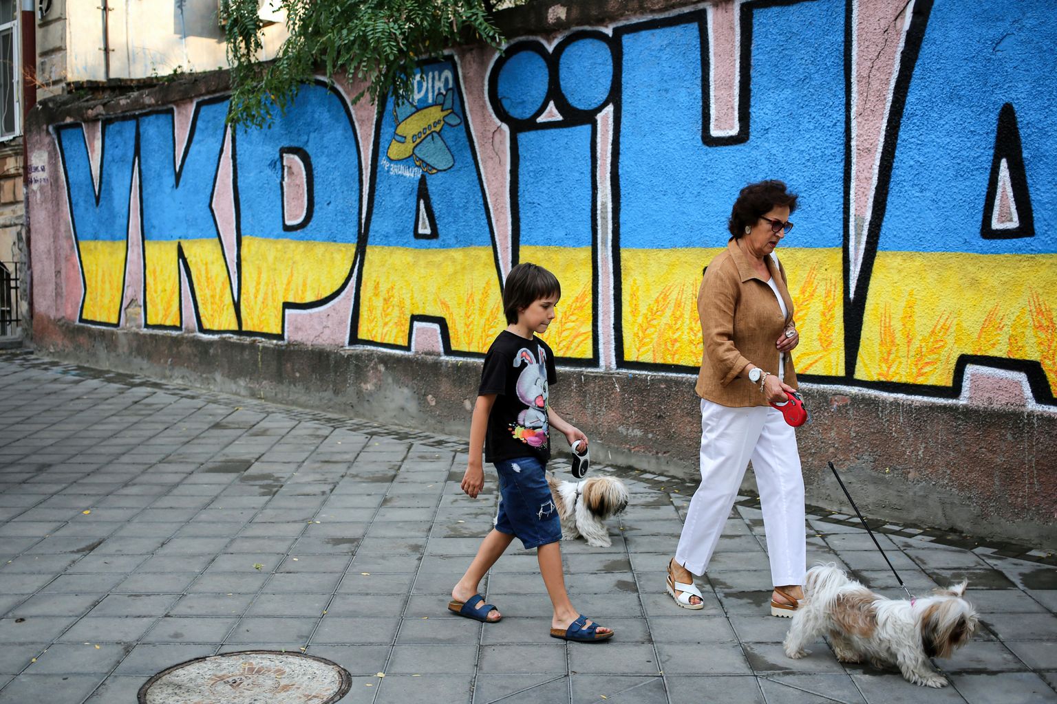 Одесса, Украина, 11 августа 2022 года. Женщина и мальчик с собаками на поводке проходят мимо стены с надписью "Украина. Мечта не может быть разрушена".