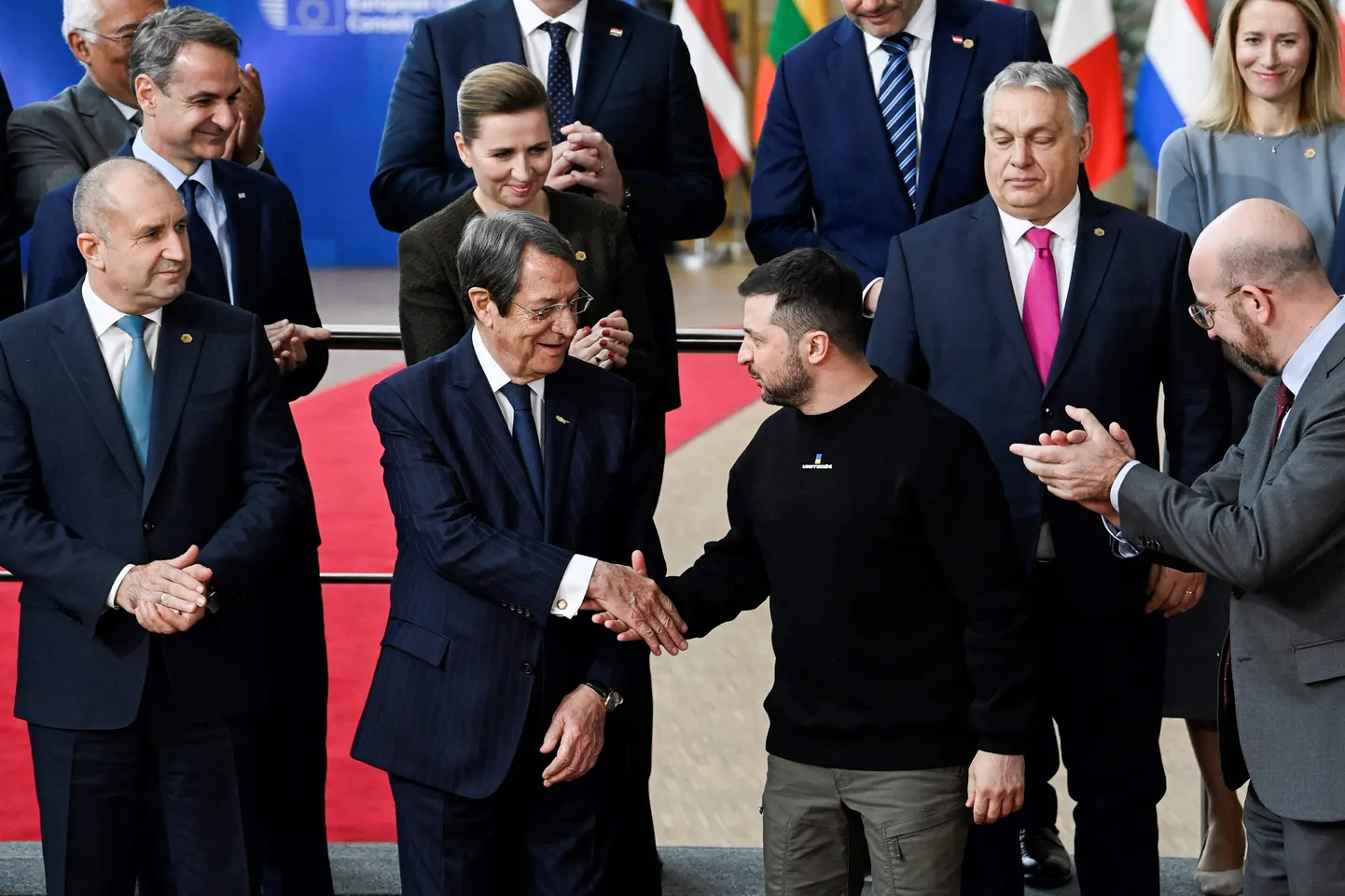 Ukraina president Volodõmõr Zelenskõi visiidil Brüsselisse, kus ta ühisfoto tegemise eel kätleb Küprose presidendi Nikos Anastasiadesega, tema kõrval aplodeerib Euroopa Ülemkogu alaline eesistuja Charles Michel ning tema õla taga Ungari vastuoluline peaminister Viktor Orbán.