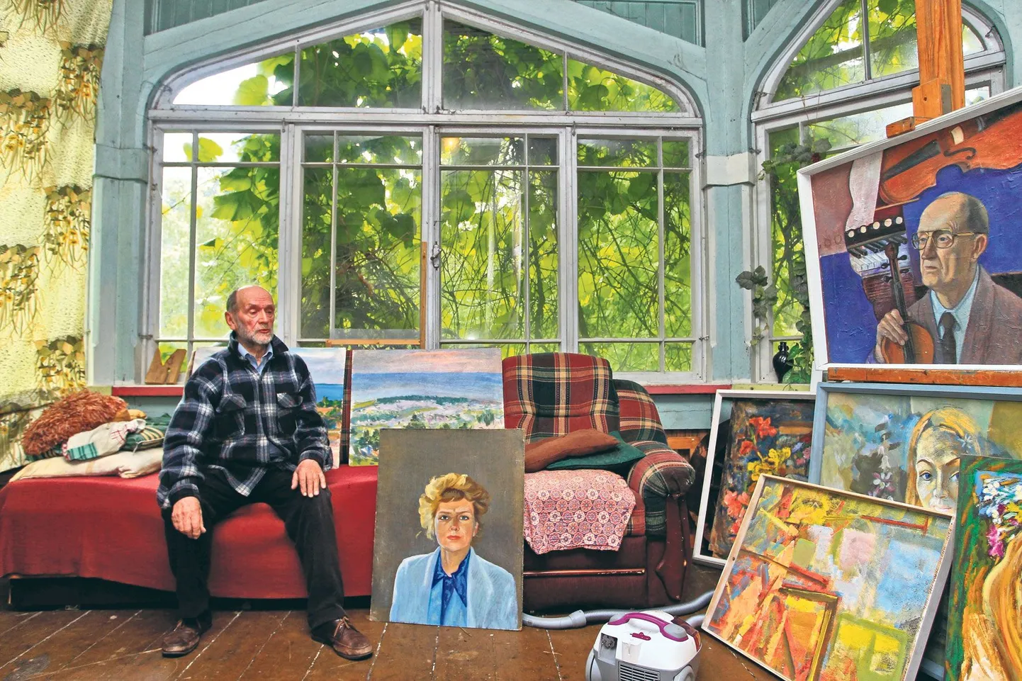 Jüri Šestakov istub oma ateljees diivanil. Muude maalide hulgas on Vanemuise orkestri kunagise esimese viiuli Eduard Poolakese (paremal ülal) ja teatrikohviku omaniku Olga Aasavi (keskel põrandal) portree.