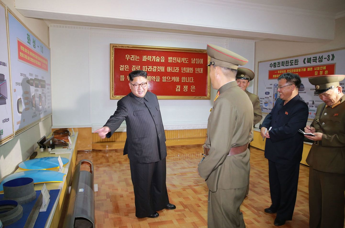 Kim Jong Un külastamas tahkel kütusel töötavate raketimootorite tehast. Kimist vasakul ja paremal on uute rakettide diagrammid.