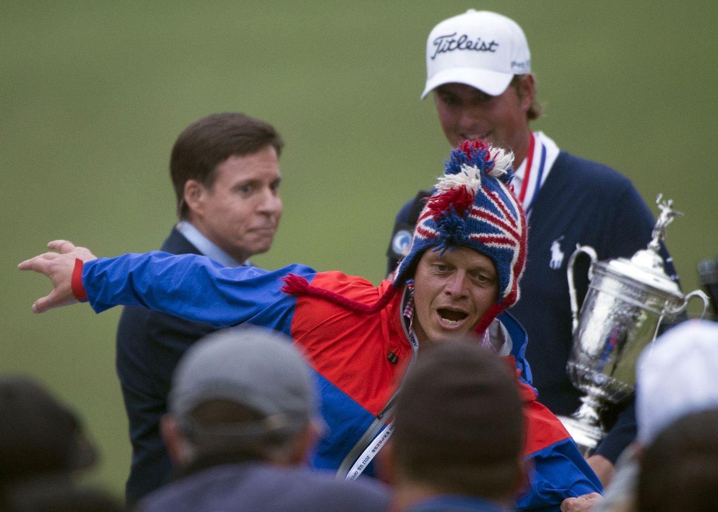 Linnuhäält tegev mees segas golfi US Openi autasustamist. Taustal on võiduintervjuud andev turniirivõitja Webb Simpson (valge mütsiga).