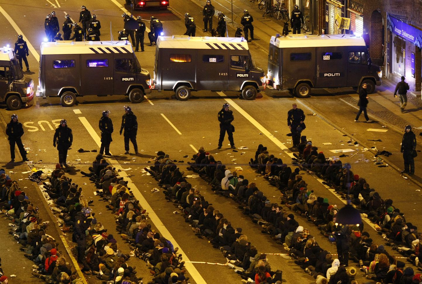 Vahistatud demonstrandid istuvad Kopenhaagenis asfaldil ja neid ümbritsevad politseinikud.