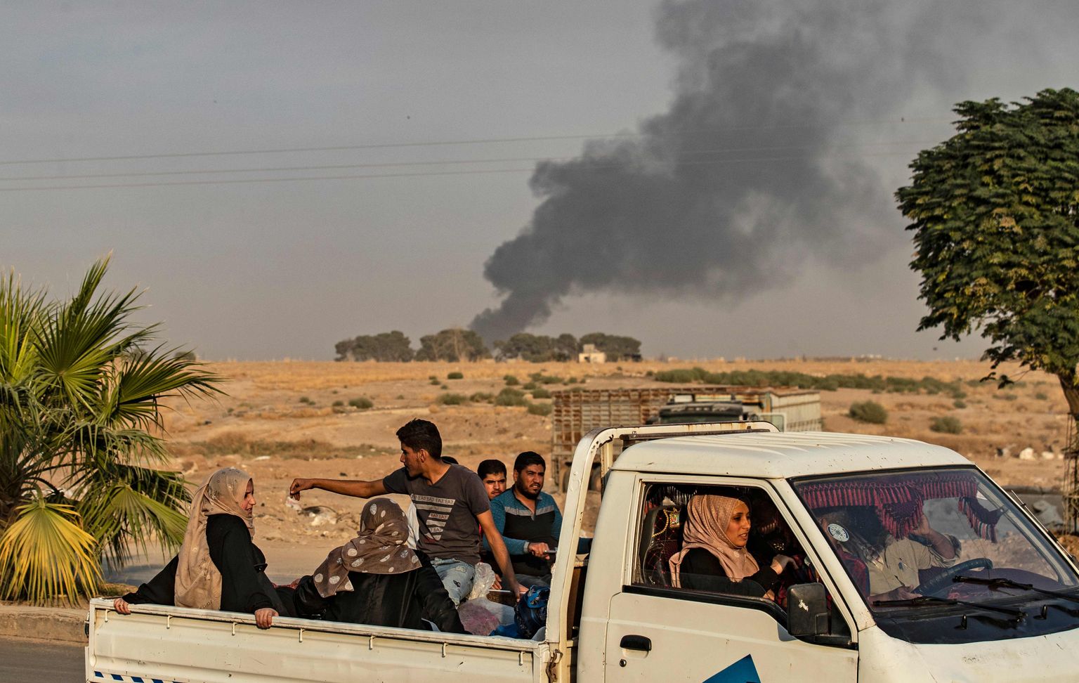 Civilians ride a pickup truck as smoke billows following Turkish bombardment in the northeastern town of Ras al-Ain in Syria's Hasakeh province along the Turkish border on October 9, 2019. - Turkey launched an assault on Kurdish forces in northern Syria with air strikes and explosions reported along the border. President Recep Tayyip Erdogan announced the start of the attack on Twitter, labelling it "Operation Peace Spring". (Photo by Delil SOULEIMAN / AFP)