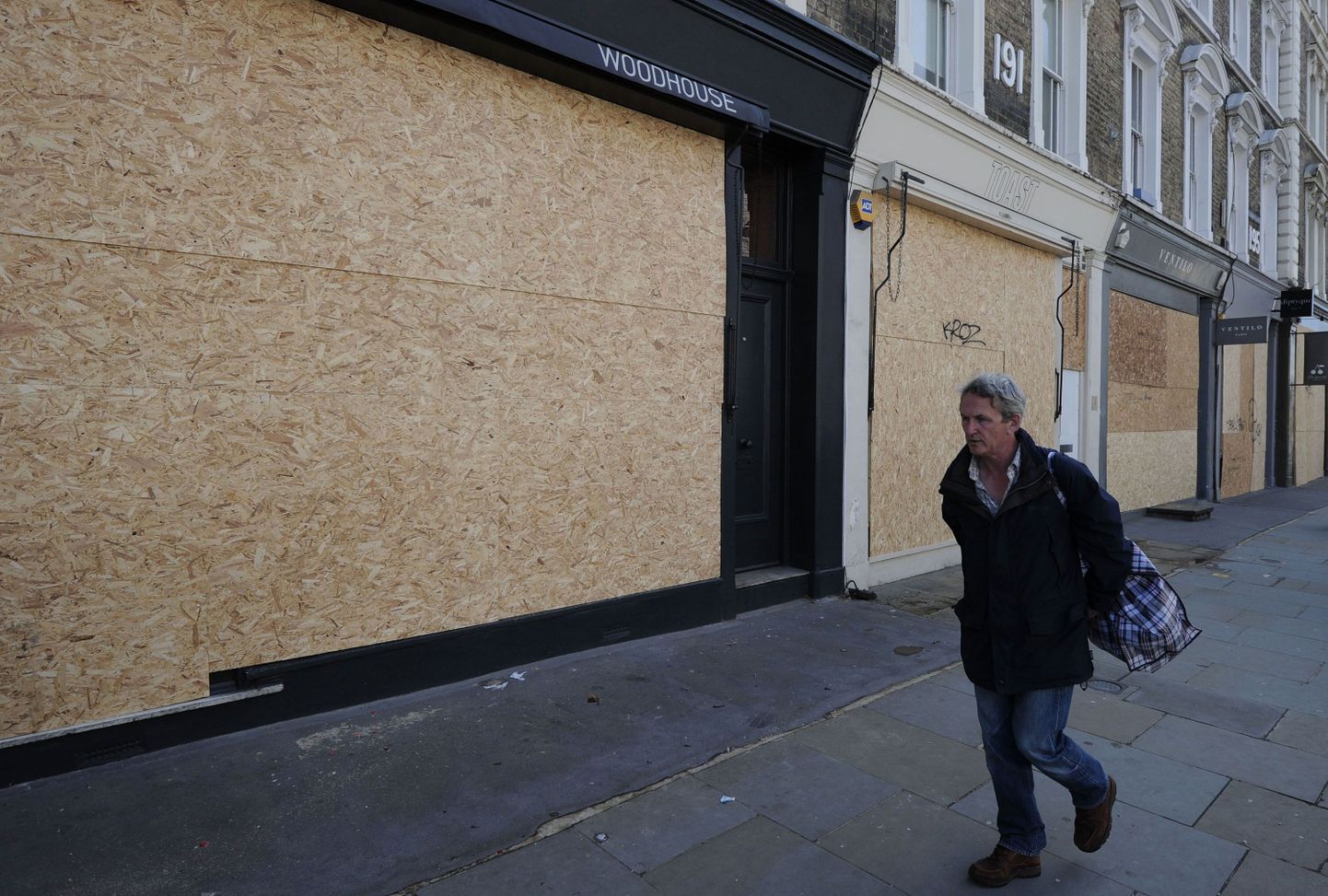 Mees jalutab Londonis Notting Hilli rajoonis mööda kauplustest, mille aknad on ettevaatuse mõttes kinni kaetud.