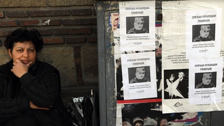 Kāda sieviete sēž blakus Ratko Mladiča dzimšanas dienai veltītiem plakātiem ar tekstu: "Daudz laimes dzimšanas dienā, ģenerāli! Paldies, ka kavē mūs no integrācijas Eiropā" 