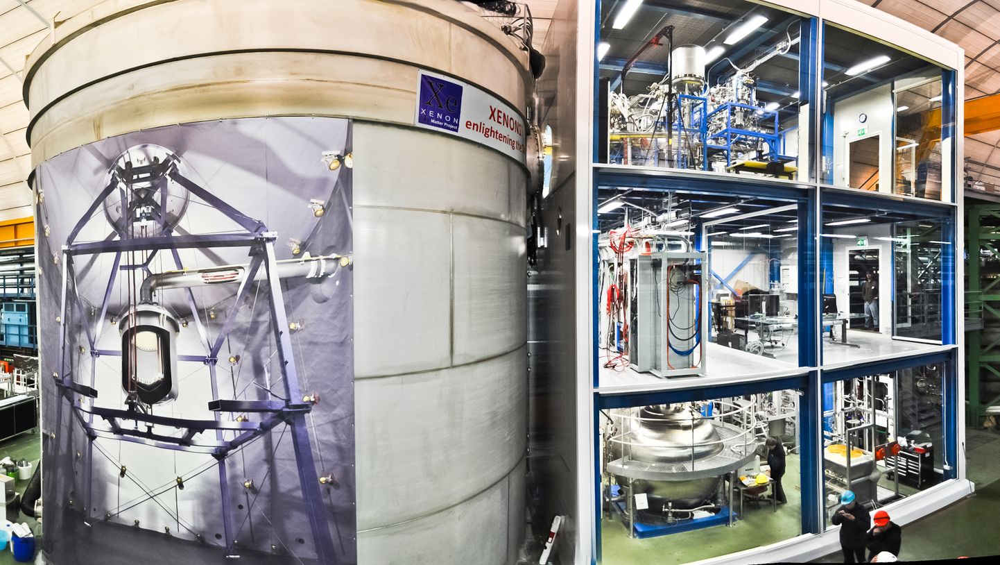 Itaalias maa-aluses Gran Sasso laboris asuv XENON1T eksperiment väljast vaadates. Vasakul on näha detektormahuti, mille küljel oleval plakatil seisab: «XENON1T: tumedust valgustades». Paremal on detektori teenindusmoodul.