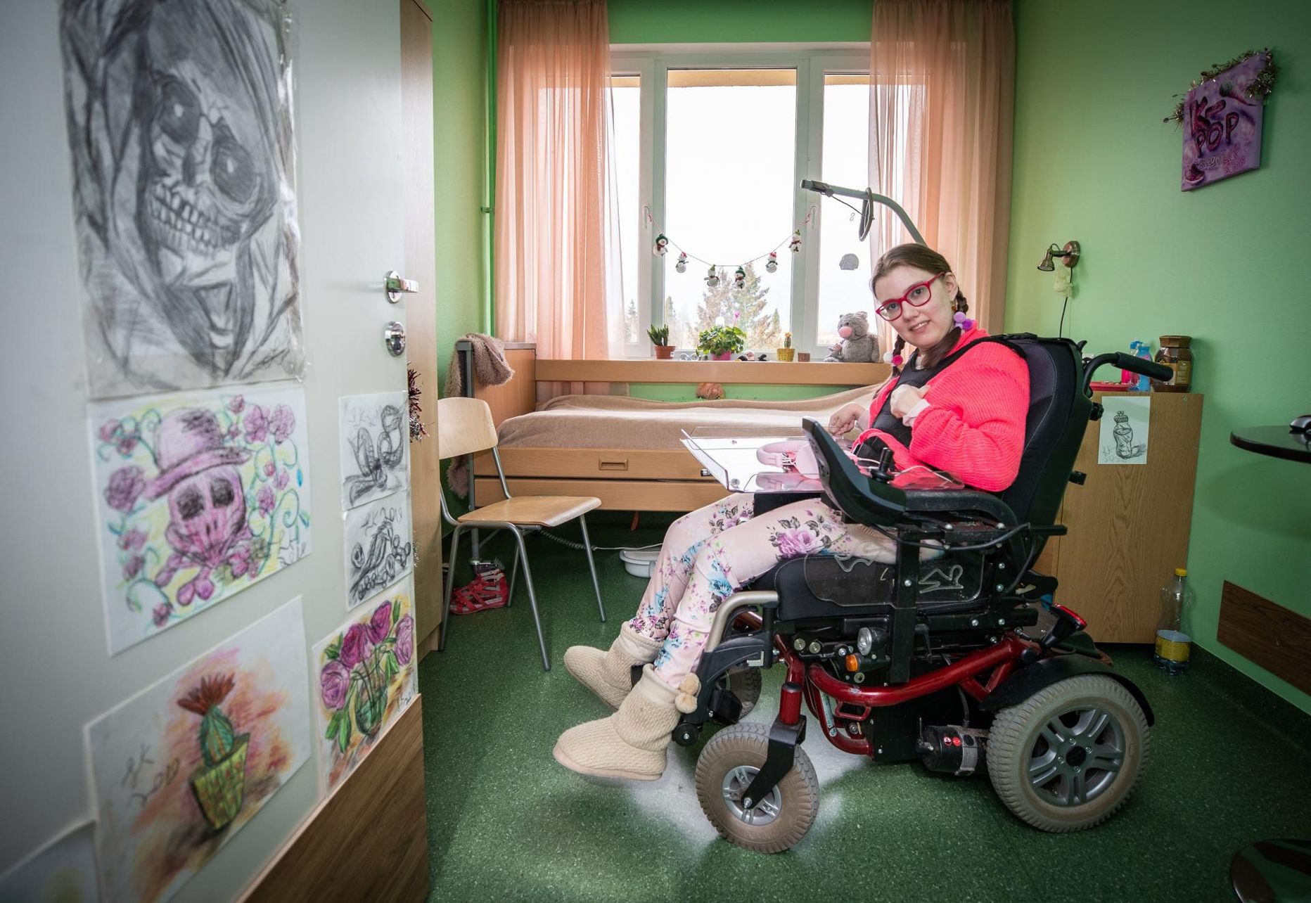 Loretta Kruusimäe (23) oma roosaga tembitud elamises Kanepi hooldekodus, seinal ripuvad tema joonistused. Tal on raamatupidaja kutse ja soov tööd teha.