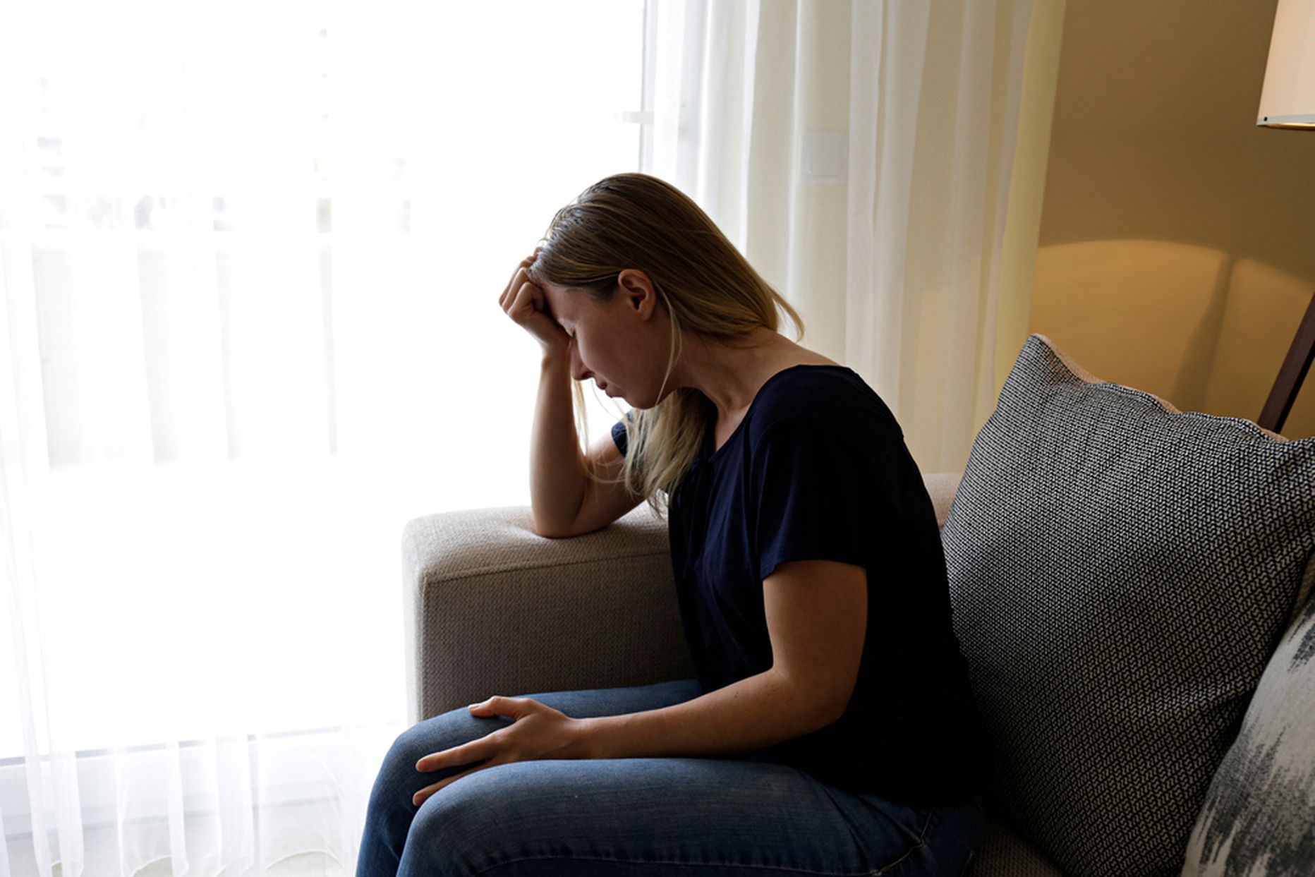 Depressed single woman sitting at home due to worldwide quarantine lockdown. Portrait of lonely stressed out female alone in her bed. Close up, copy space, background.