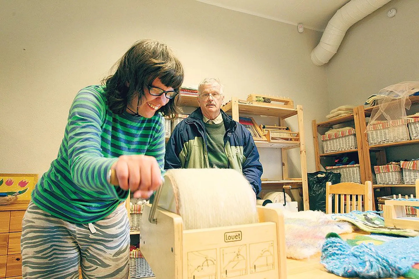 Maria-Elisabeth Ranne näitab, kuidas ta kraasimasinaga ümber käib. Taga vanaisa Raivo Ran­ne, kes saadab tüdrukut sageli ning kes on tugikeskuse keraamikakot­ta teinud savikedra.