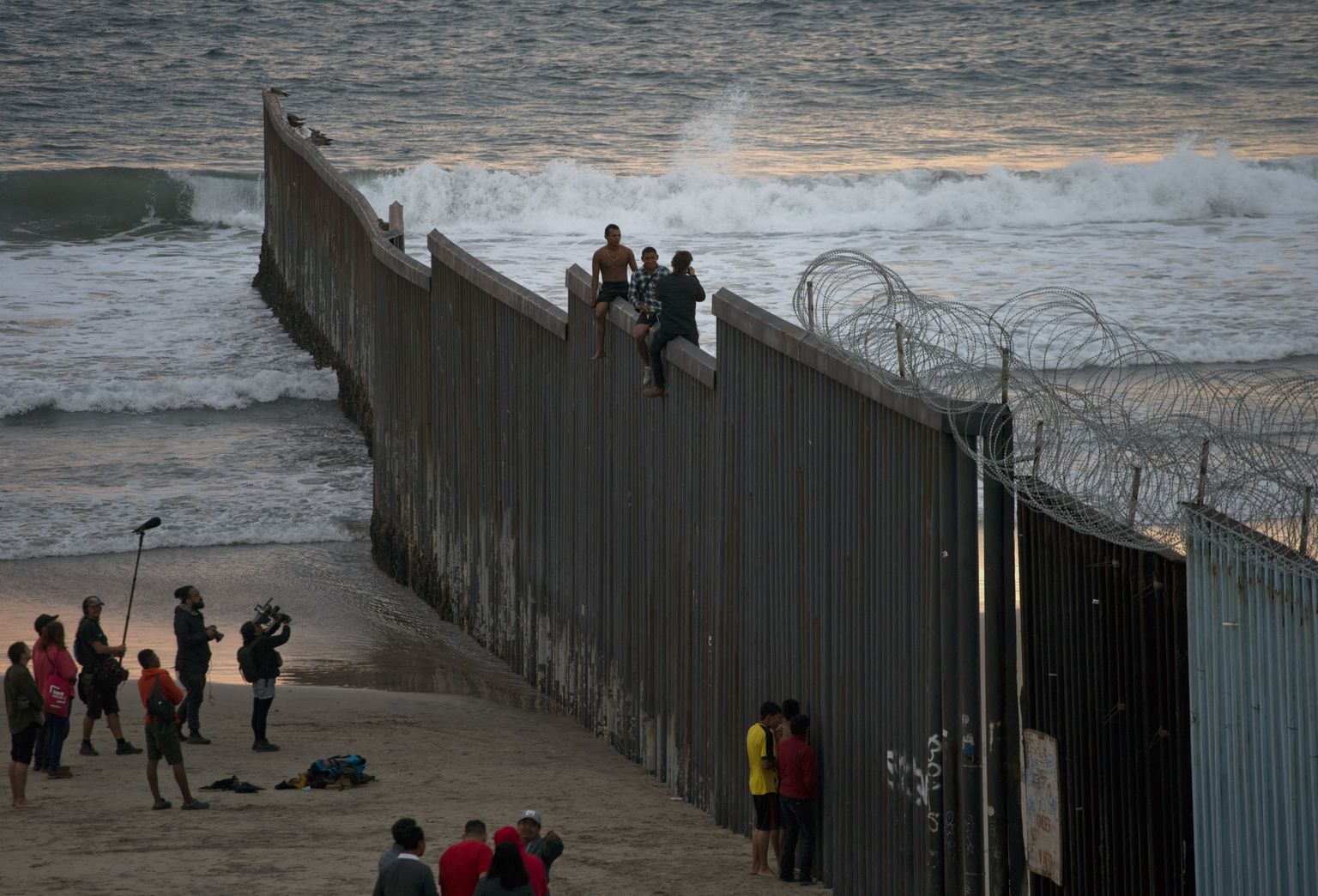 Hondurase migrandid poseerivad fotol Tijuanas, istudes Mehhikot ja USAd eraldaval piiritaral.