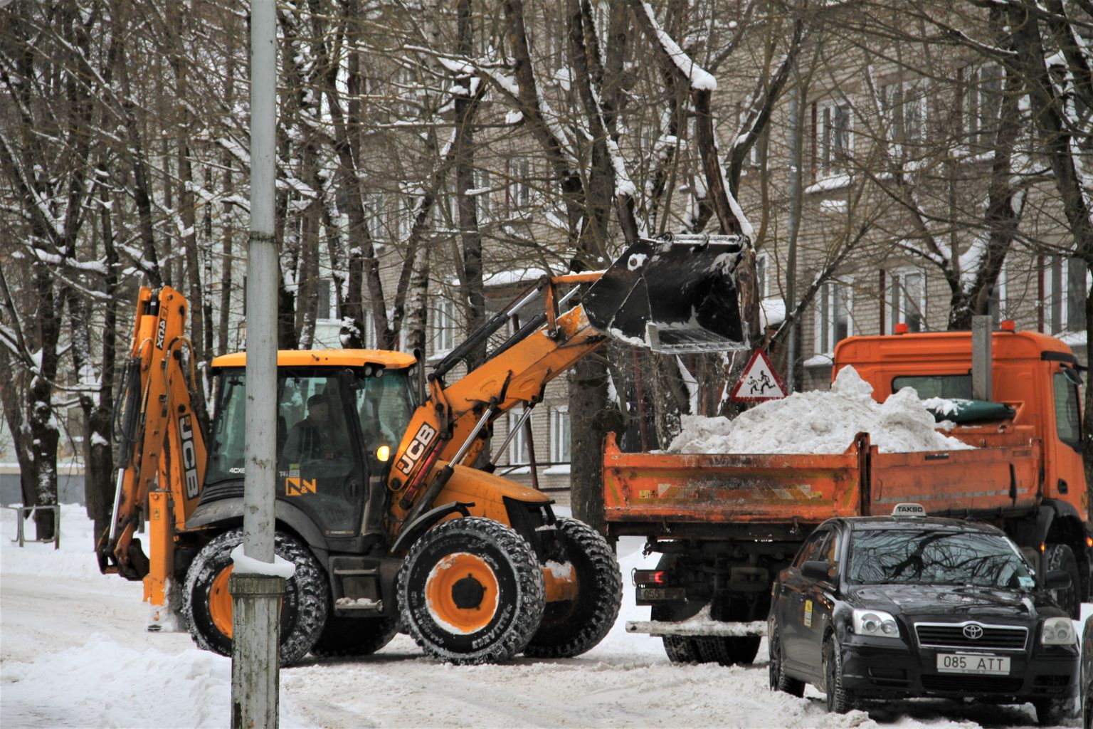 Тракторист грузит собранный с дороги снег для вывоза из города.