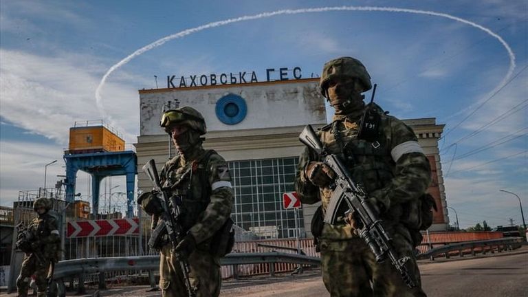 Двое солдат с автоматами на фоне бетонного здания, на котором написано «Каховская ГЭС».