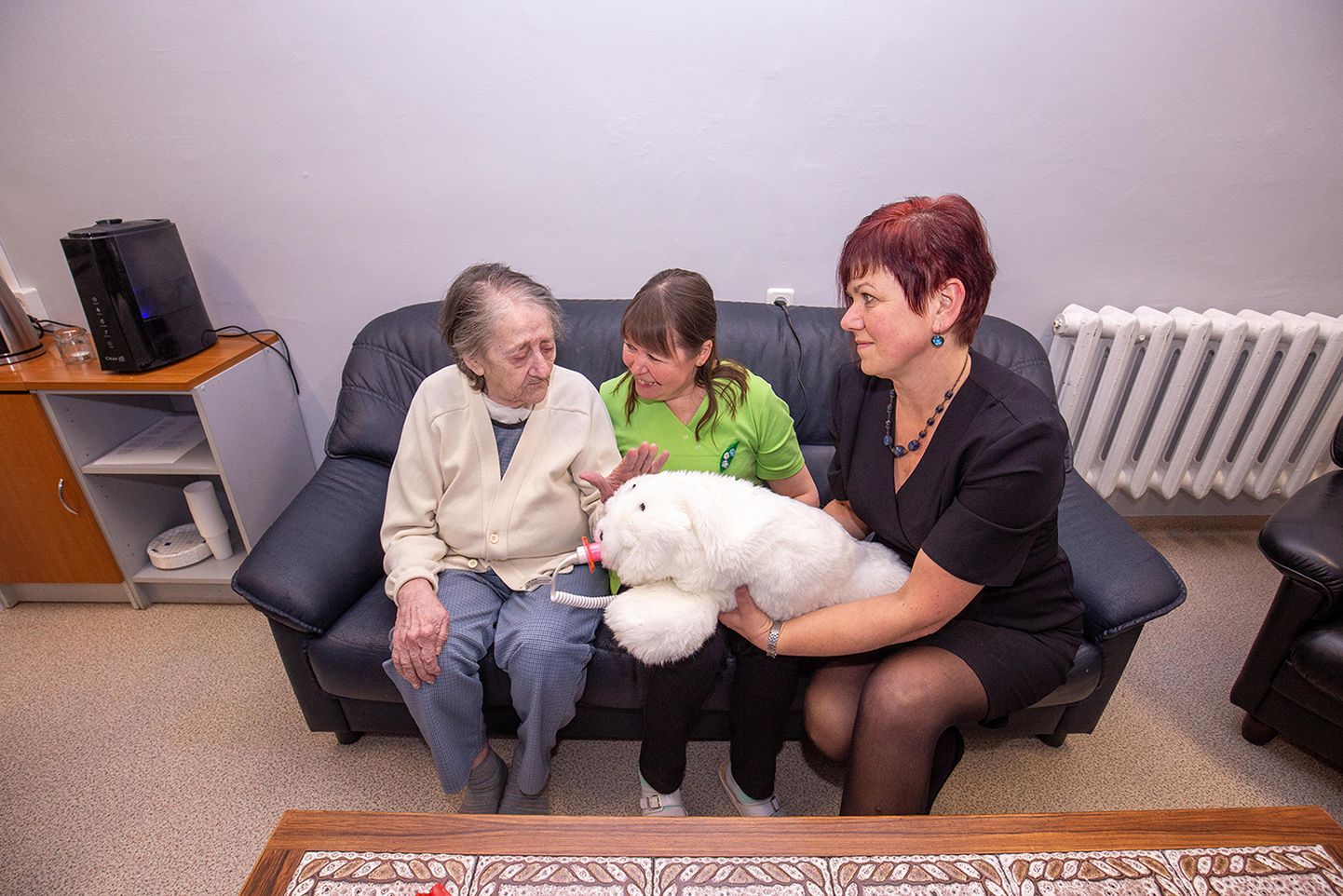 «Nii pehme, õrnpehme!» kiidab Selma (vasakul) vanemhooldajale Sirle Liidresele ja Koeru hooldekeskuse juhatajale Terje Tederile pehmet ja valge karvaga hülgepoega paitades. See on teraapiarobot, mis reageerib puudutustele ja häälele neile omasel moel.