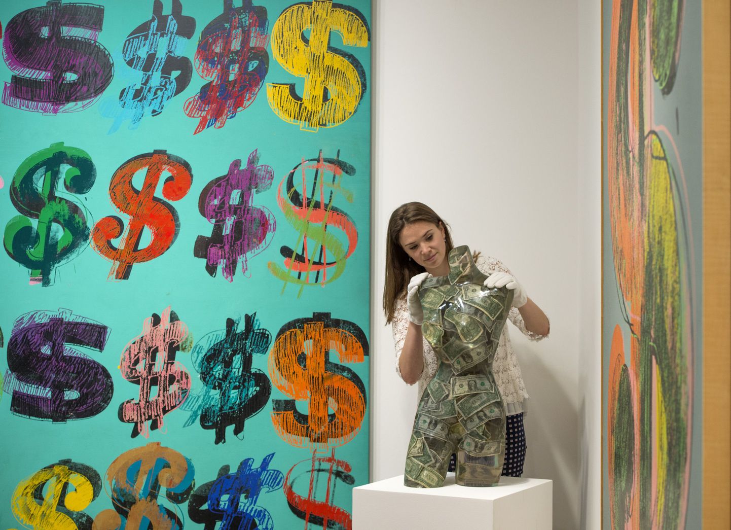 A gallery assistant poses with 'Venus aux dollars, 1970' by Arman, estimated ÃÂ£16-ÃÂ£22,000, beside 'Dollar Signs, 1981' by Andy Warhol, estimated at ÃÂ£4.5-ÃÂ£6.5 million, (left) during the press preview of 'To The Bearer On Demand', a private collection of 21 works inspired by the US Dollar by artists including Andy Warhol at Sotheby's, London.