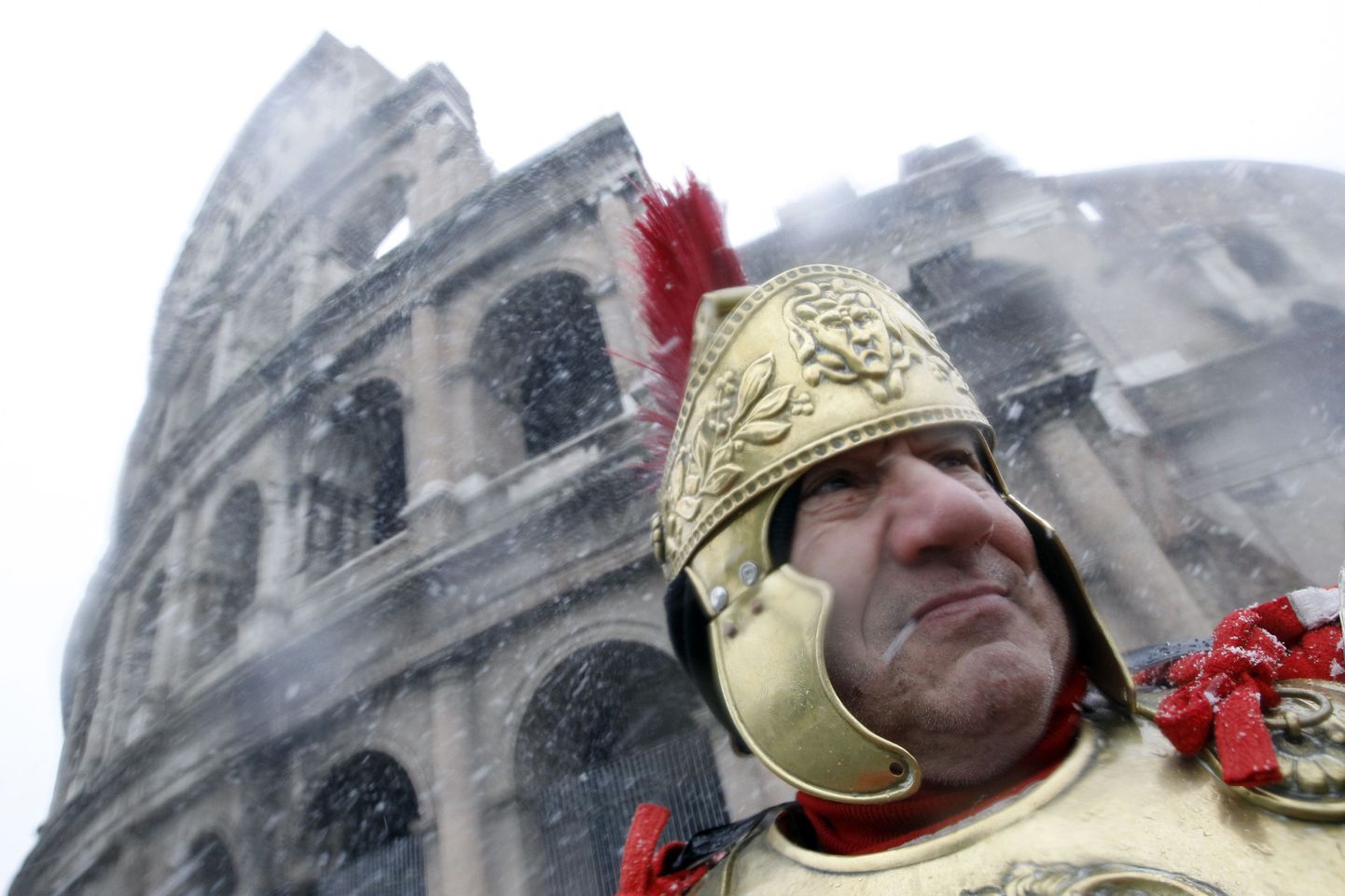 Rooma tsentuurioniks riietunud mees seismas lumesajus Colosseumi ees.