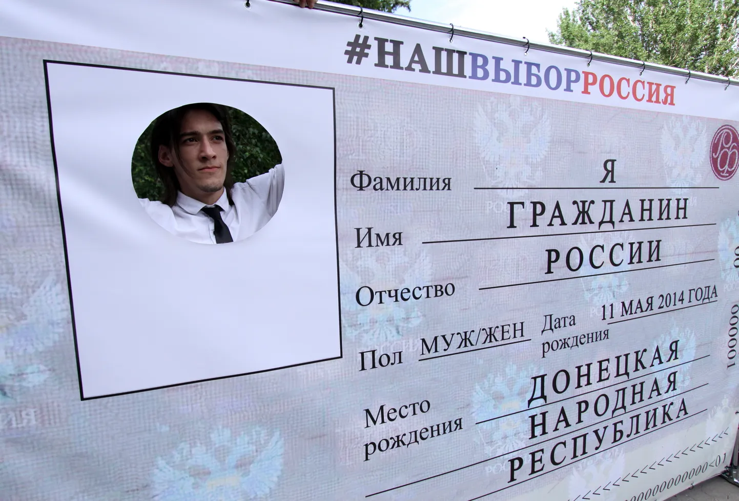 Житель Донецка (Украина) позирует для фото, выглядывая через окошко макета российского паспорта. 12 июня 2019 года.