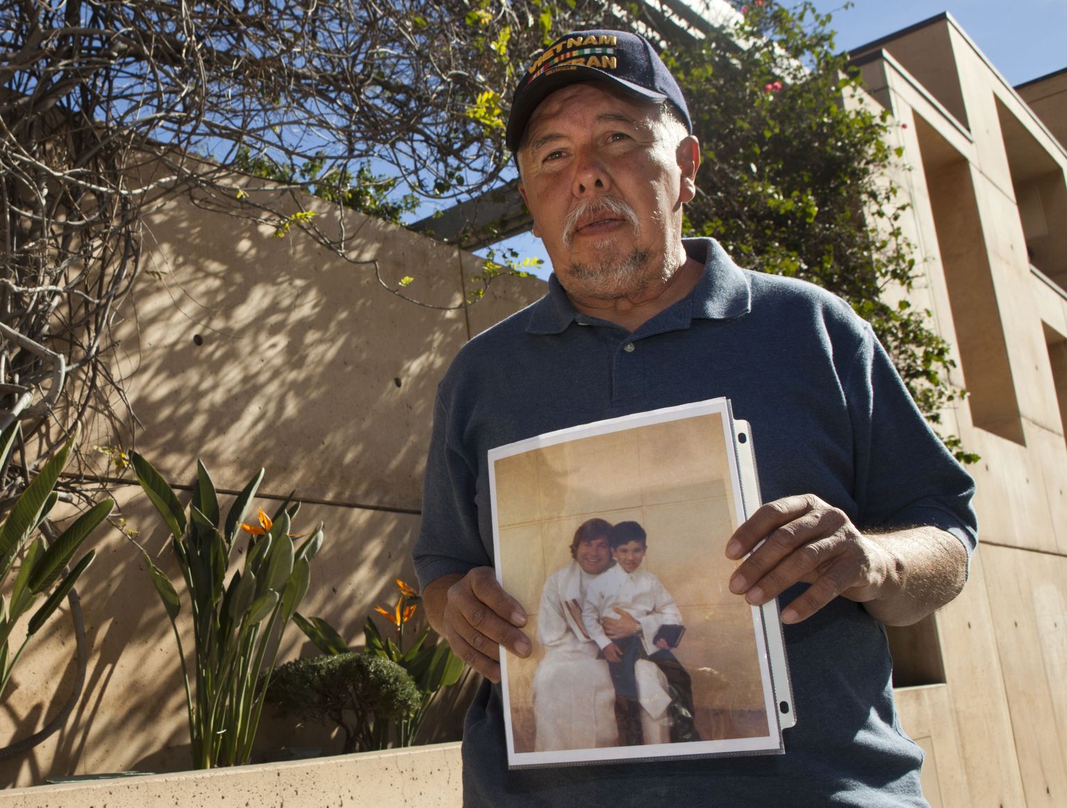 Frank Zamora (67) näitab pilti oma 8-aastasest pojast Dominicist, kes istub last ahistanud preestri Michael Stephen Bakeri kõrval.