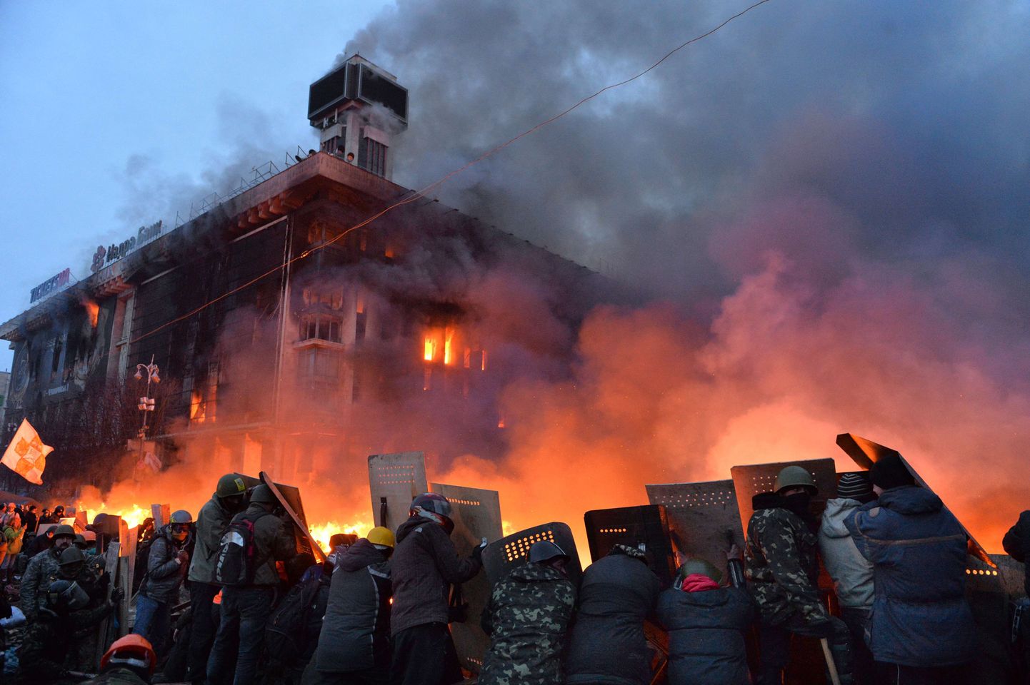 Ukraina valitsusvastased kaitsevad end  kilpidega miilitsatöötajate eest. Tagaplaanil paistab põlev ametiühingute maja.