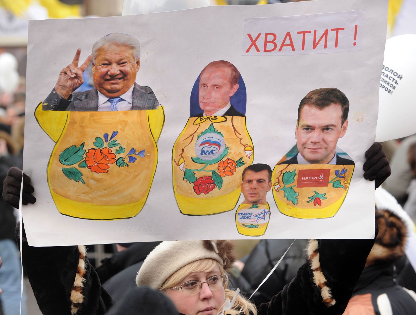 Plakat «Aitab!», kus matrjoškadena on kujutatud Boriss Jeltsinit, Vladimir Putinit, Dmitri Medvedevit. Kõige ees on tibatilluke Mihhail Prohhorov.