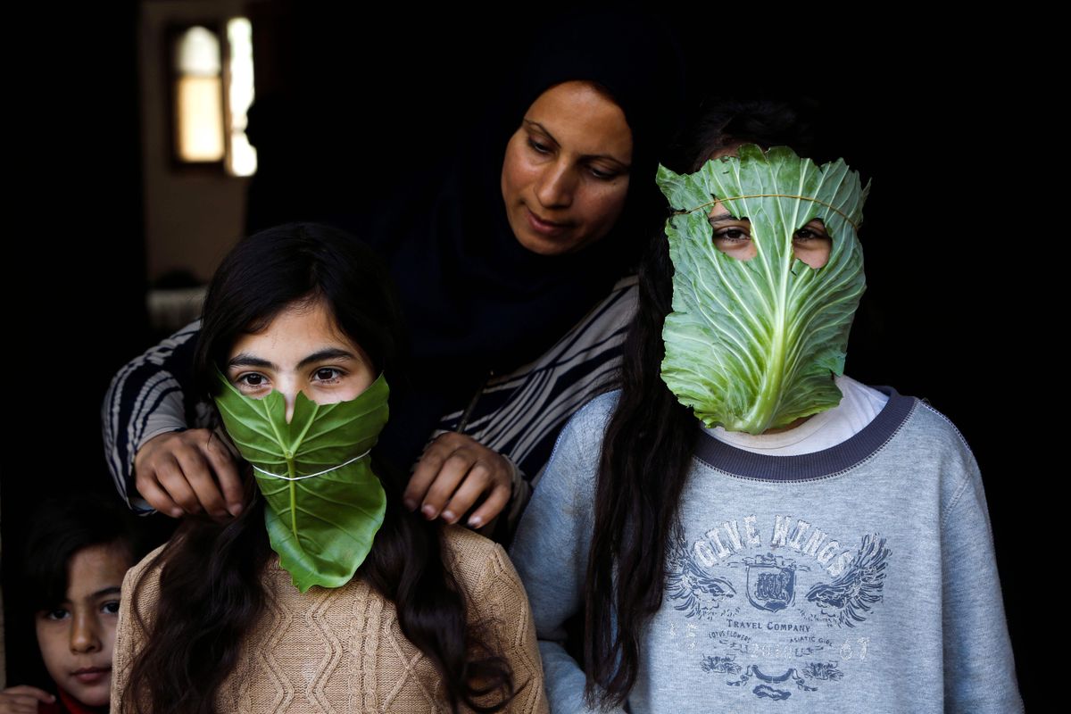 Palestīniešu sieviete saviem bērniem veido improvizētas sejas maskas.