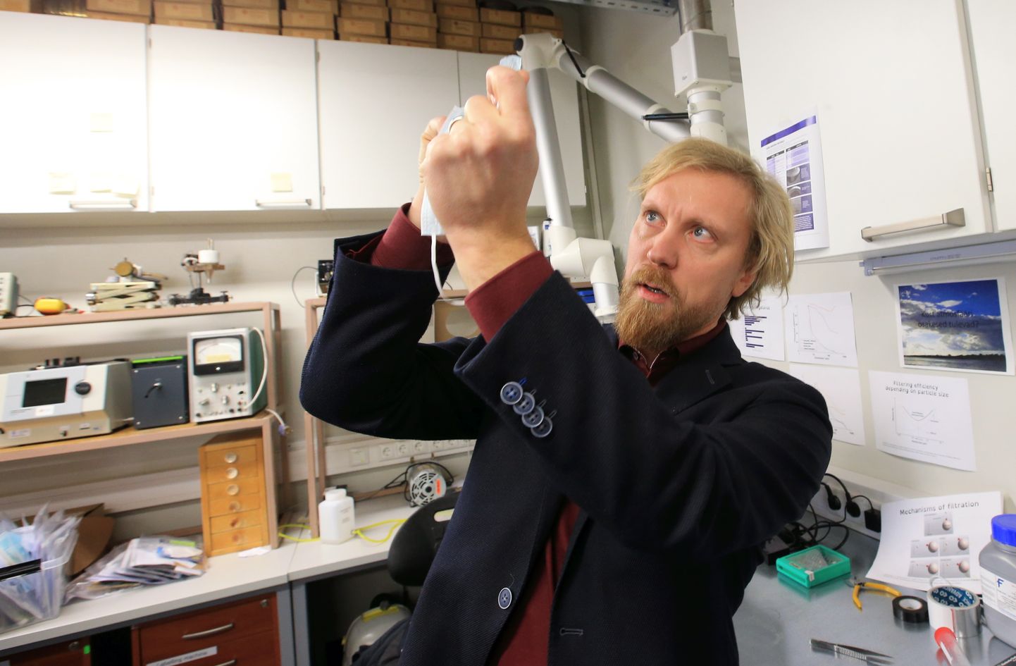 Tartu ülikooli keskkonnafüüsika professor Heikki Junninen takseerib üht meditsiinilise maski filtrit, millest läbi vaadates midagi ei paista - vaid ühtlane piimjas kuma. Ühekordsed meditsiinilised maskid on ühed kõige paremad aerosooliosakeste kinnihoidjad.