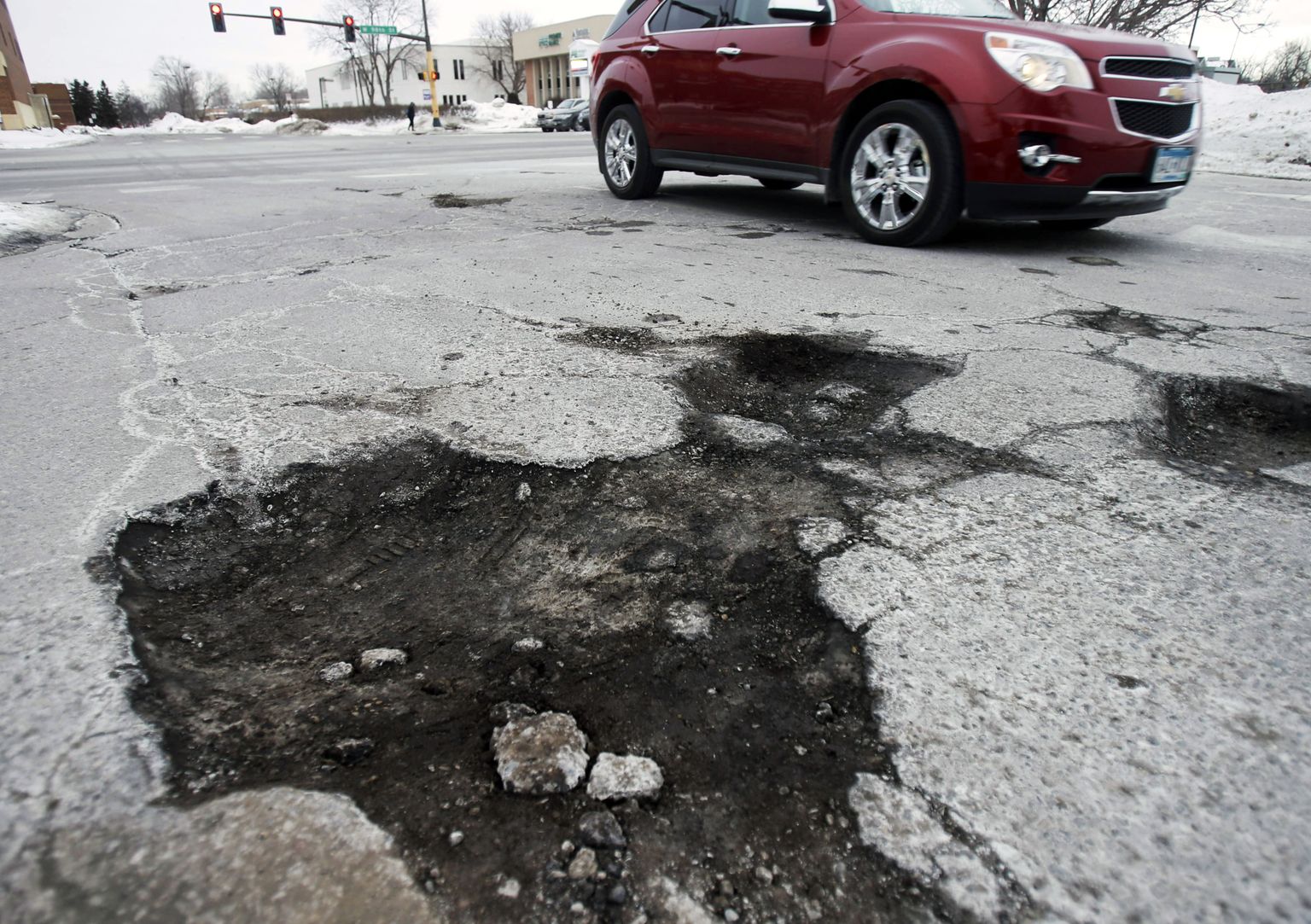 In this Tuesday, Feb. 11, 2014 photo, a driver navigates past several potholes in Bloomington, Minn. The relentless cycle of snow and bitter cold this winter is testing the skeletons of steel and cement on which communities are built. Pipes are bursting in towns that are not used to such things, and roads are turning into moonscapes of gaping potholes big enough to snap axles of passing vehicles. (AP Photo/Jim Mone) / TT / kod 436