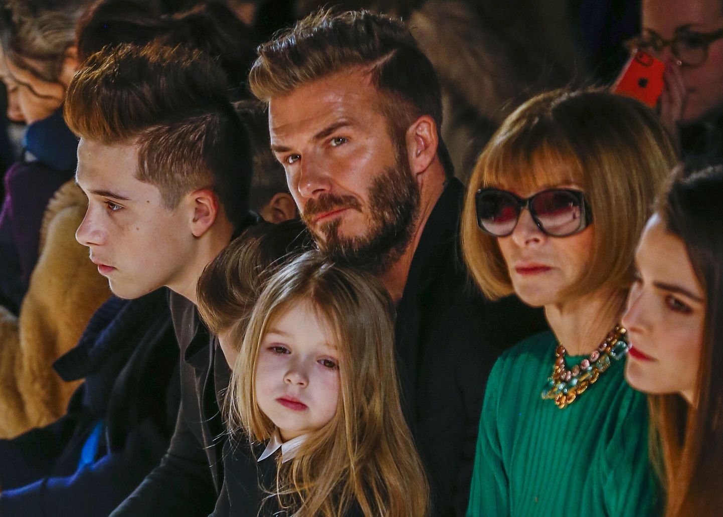Former England captain David Beckham sits next to U.S. Vogue editor Anna Wintour (2nd R) with his daughter, Harper, on his lap and son Brooklyn (L) during a presentation of the Victoria Beckham Fall/Winter 2015 collection during New York Fashion Week February 15, 2015. REUTERS/Lucas Jackson (UNITED STATES - Tags: FASHION SOCIETY ENTERTAINMENT SPORT)