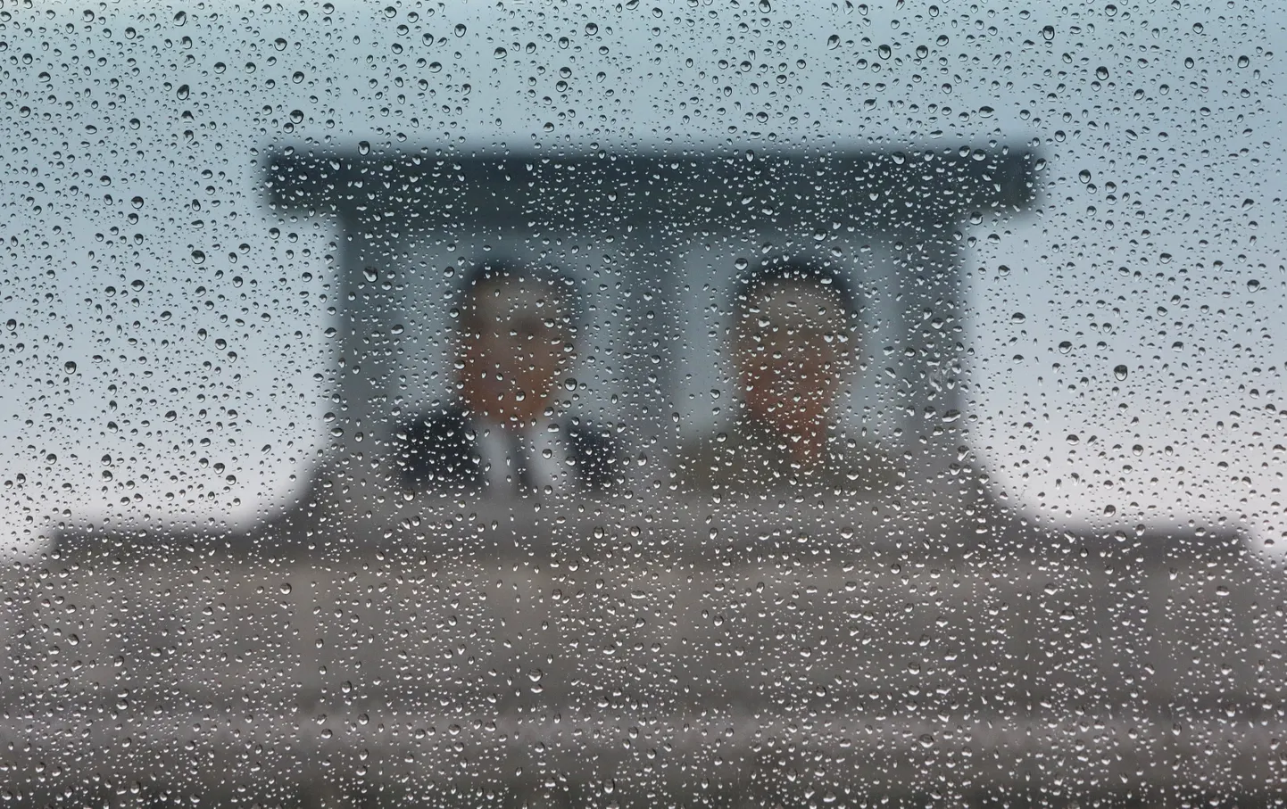 Vihm varjutab bussiakna tagant paistvate Põhja-Korea rajajate Kim Jong-ili and Kim Il-sungi portreed.