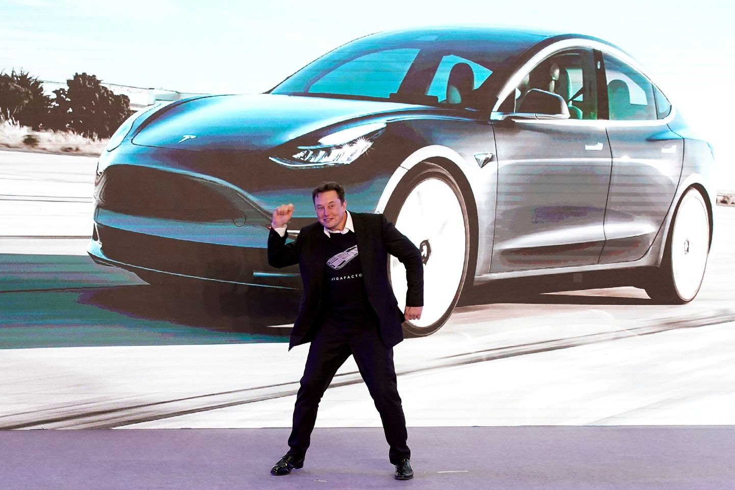 Elon Musk  tantsib Hiinas valmistatud Model 3 kujutisega ekraani ees Šhangais.