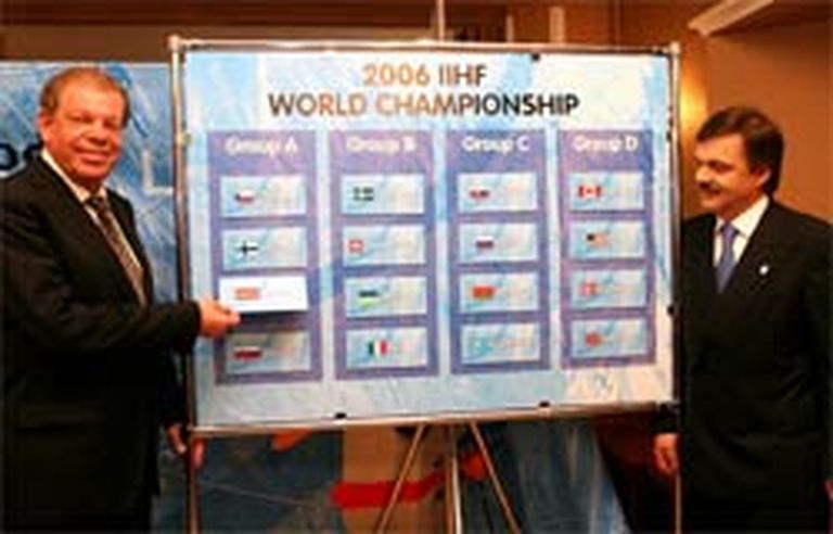 Kirovs Lipmans (pirmais no kreisās) un Renē Fāzels pozē pie shēmas, kur redzams komandu sadalījums pa grupām. Lipmans akcentē Latvijas pozīciju - kopā ar pasaules čempioniem jau trešo gadu pēc kārtas... 