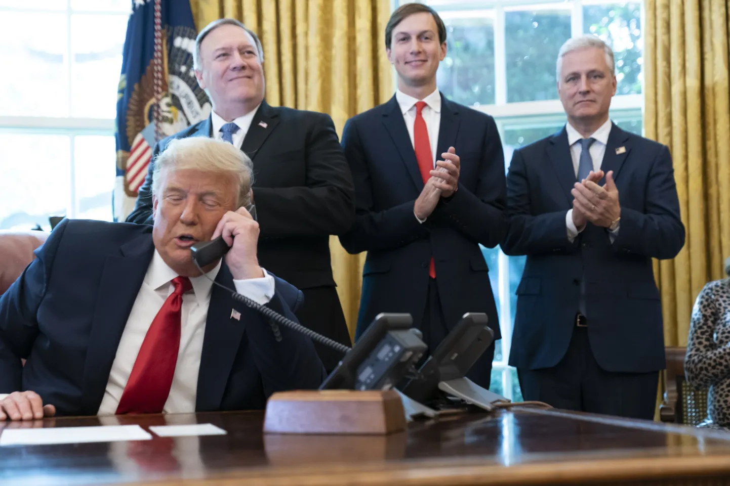 Дональд Трамп звонит из Овального кабинета, а государственный секретарь Майк Помпео (слева), старший советник Белого дома Джаред Кушнер и советник по национальной безопасности Роберт О'Брайен аплодируют. Архивное фото 2020 года.
