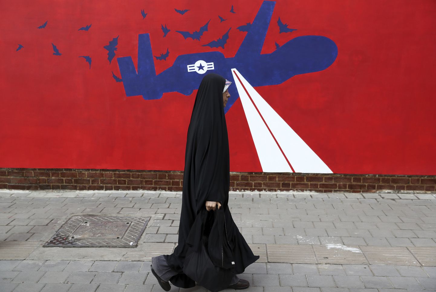 Naine kõndimas Teheranis mööda uuest pildist kunagise USA saatkonna seinal, kus näidatakse USA drooni Global Hawk allatulistamist.