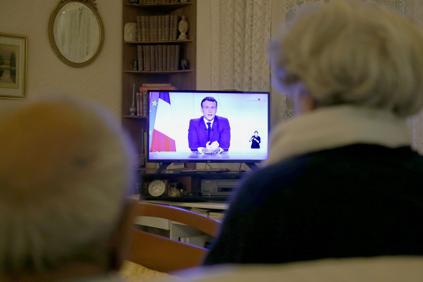 Senioru pāris televizorā skatās Francijas prezidenta Emanuela Makrona uzrunu