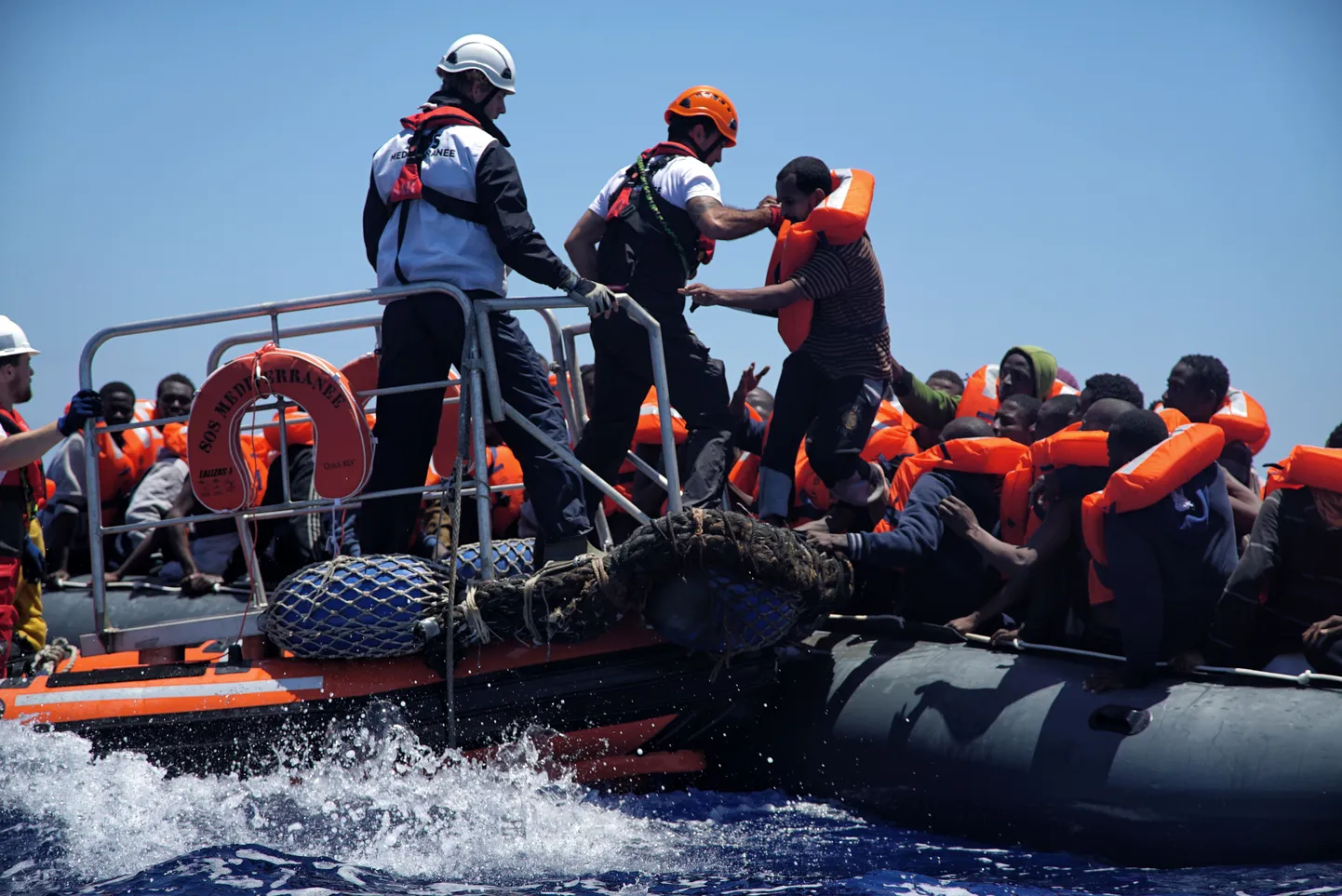 Rescue workers help migrants to disembark from a dinghy in the Mediterranean Sea, rescued by members of the aid group Medecins Sans Frontieres (MSF) and the rescue group SOS Mediterranee Rescuers of SOS Mediterranee, Thursday June 23, 2016.  The humanitarian groups distribute life jackets to the migrants in distress on the Mediterranean Sea before taking them aboard the 'Aquarius' vessel. (AP Photo/Bram Janssen)