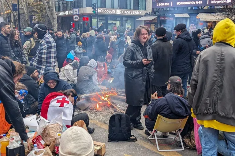 Протестующие в Тбилиси жгут костер на улице, у одного спина накрыта грузинским флагом.