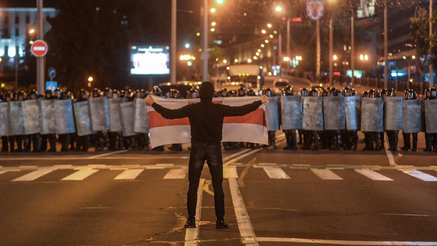 Протест - Беларусь, август 2020 года. Одинокий мужчина держит белый флаг с красной полосой перед толпой омоновцев