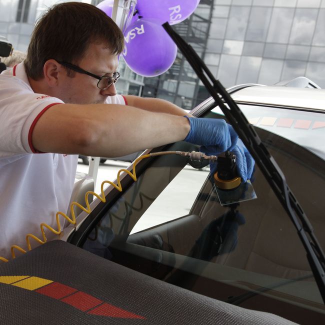 Technician performing precision work on vehicle windshield glass