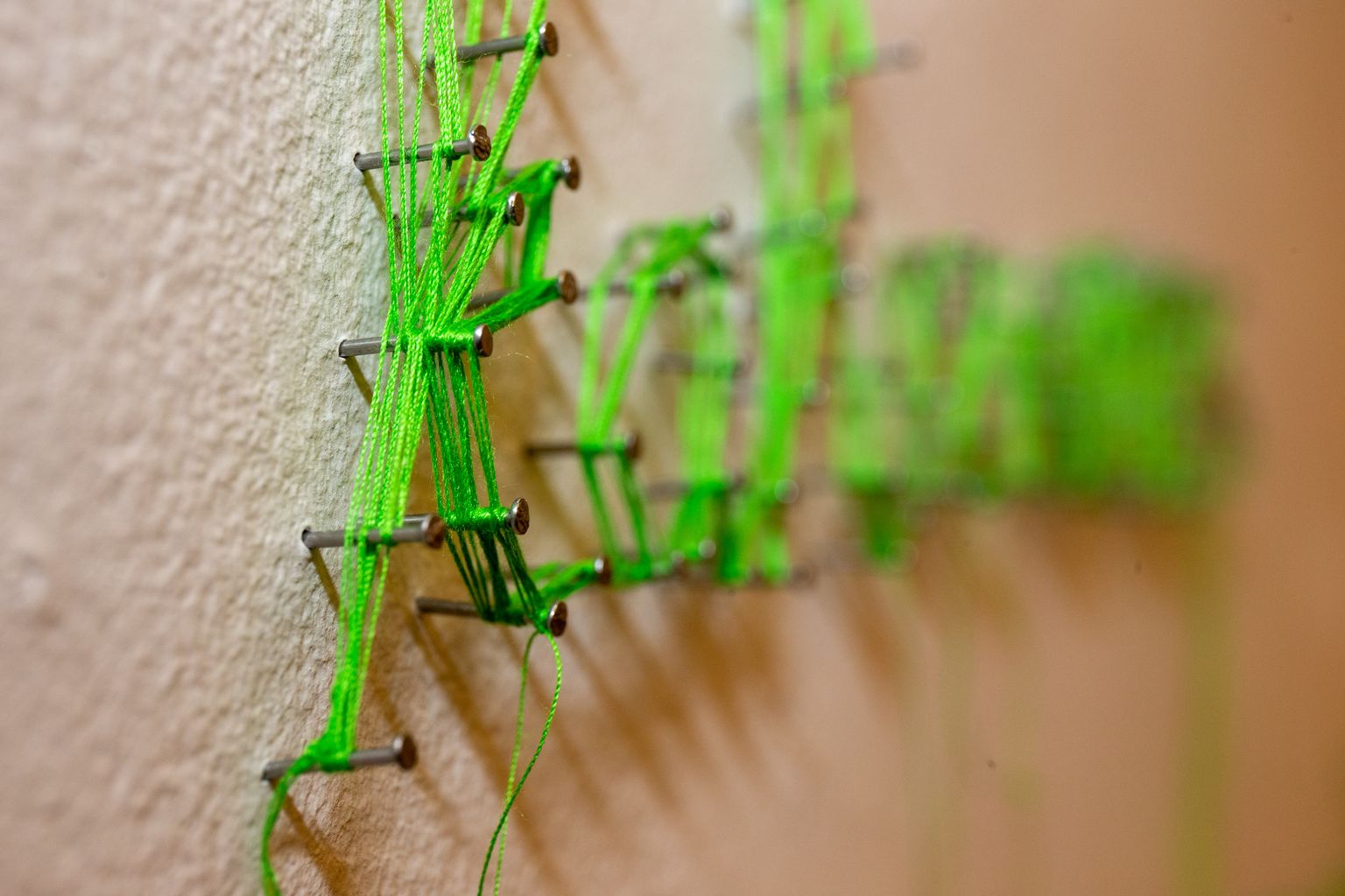 Seina löödud naelad Laura Põllu ja Katrin Väli installatsioonis "Eitus". Naelte vahel ja ümber on roheline siidniit.