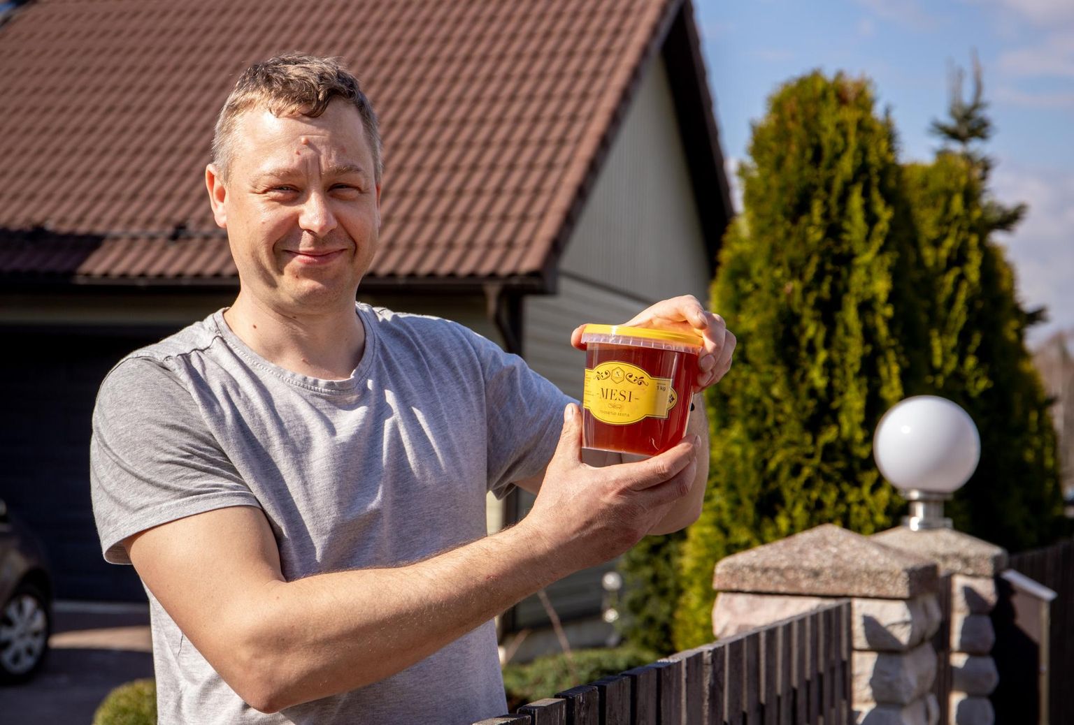 Mesindusele kui majandus­harule pühendunud turundavad ka piirkonda, nii nagu Tammiste küla mesinik ­Marek Sein, kes koduväraval seistes oma mesila logoga pange käes hoiab.