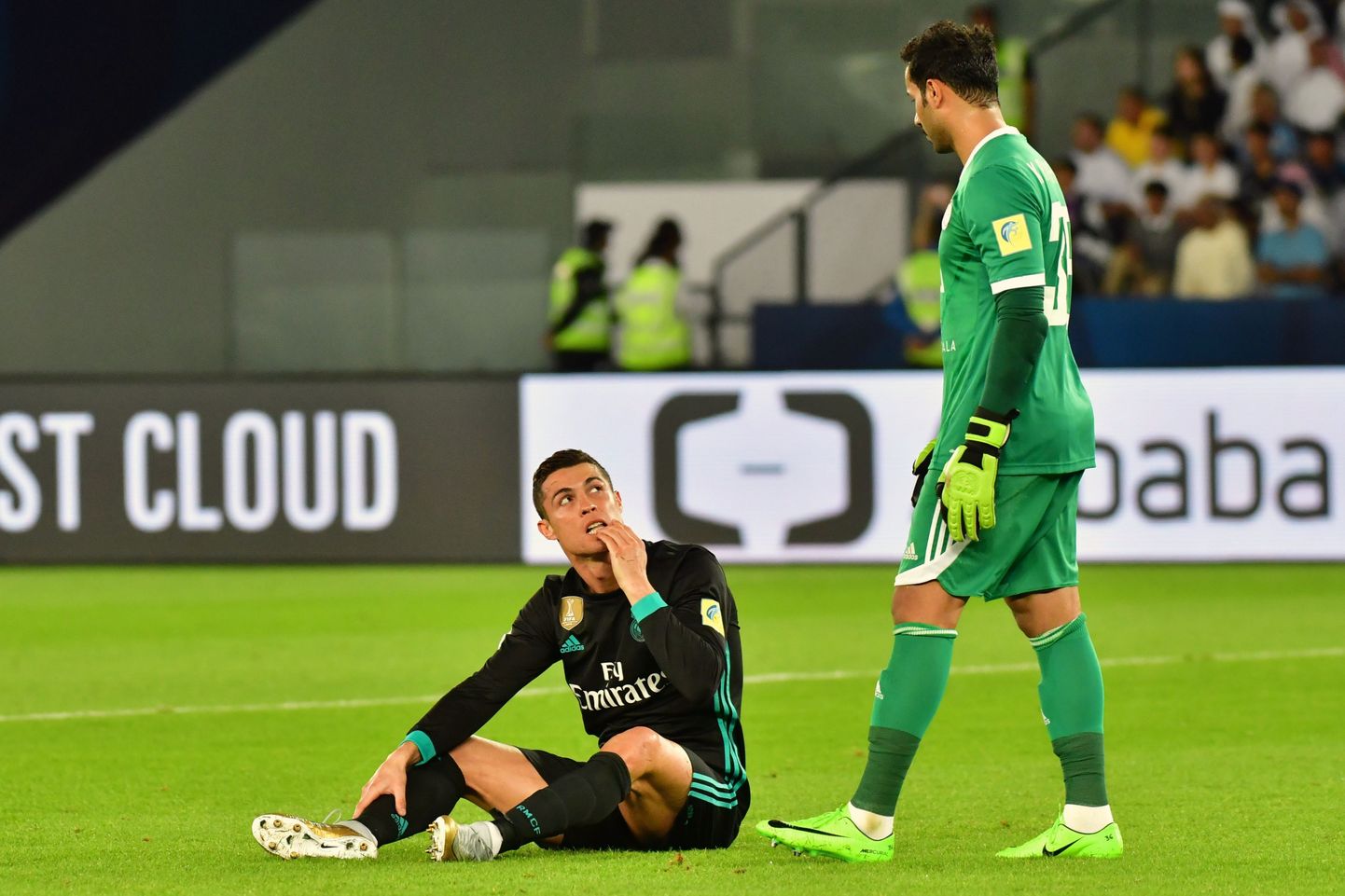 Real Madrid's Portuguese forward Cristiano Ronaldo (L) reacts after a collision with a shot as he is marked by al-Jazira's Emirati goalkeeper Khaled al-Senani  (R) during the FIFA Club World Cup semi-final match in the Emirati capital Abu Dhabi on December 13, 2017. / AFP PHOTO / GIUSEPPE CACACE
