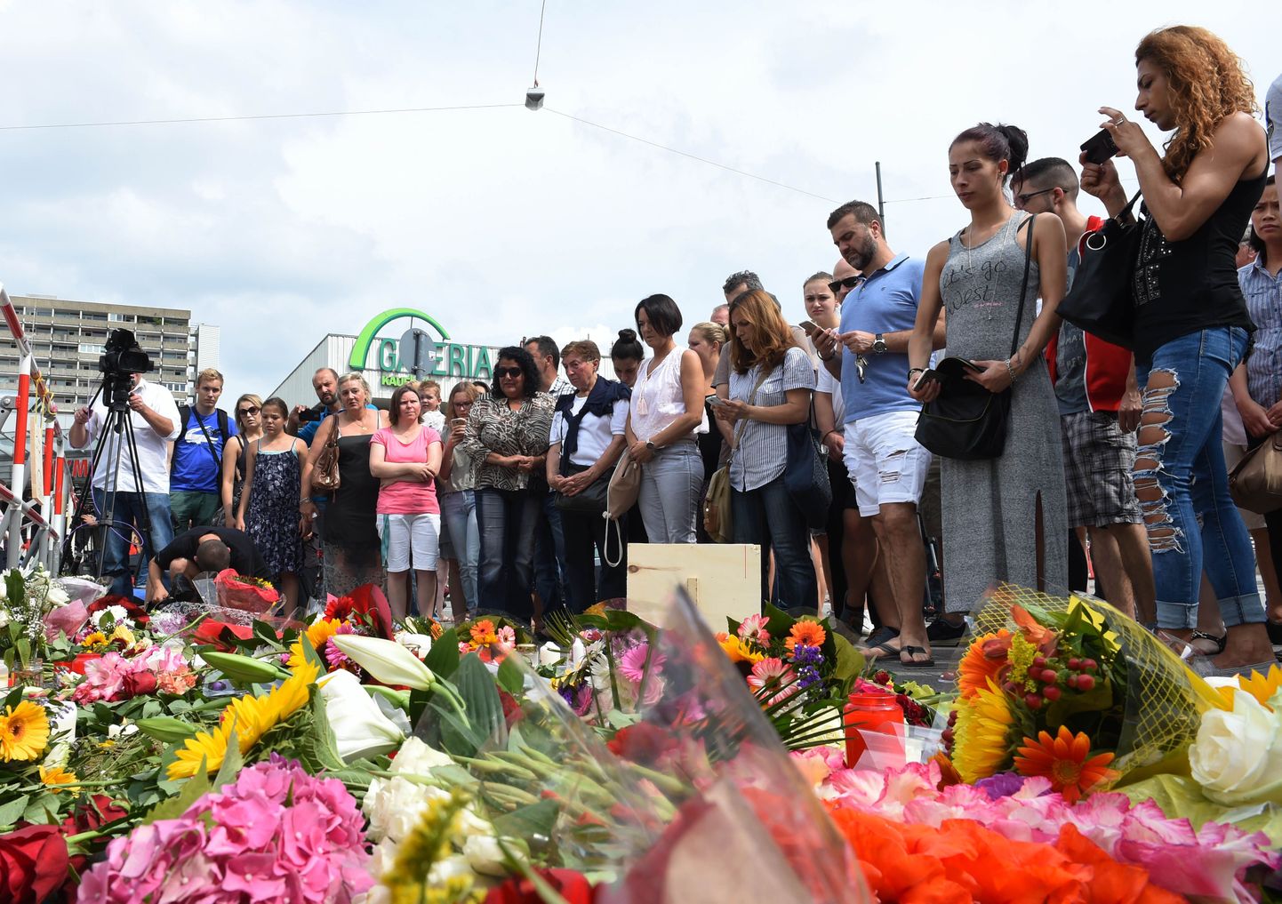 People stand next to flowers laid down on July 23, 2016 for the victims of the shooting near the Olympia-Einkaufszentrum shopping centre in Munich, southern Germany, one day after the attack.
Police were probing the motives of the lone teenage German-Iranian gunman who went on a deadly rampage at a busy Munich shopping centre, the third bloody attack on civilians in Europe in just over a week. Nine people were killed and another 16 wounded as the black-clad gunman brought terror to Germany's third largest city on Friday evening, July 22, 2016, before committing suicide. / AFP PHOTO / Christof Stache