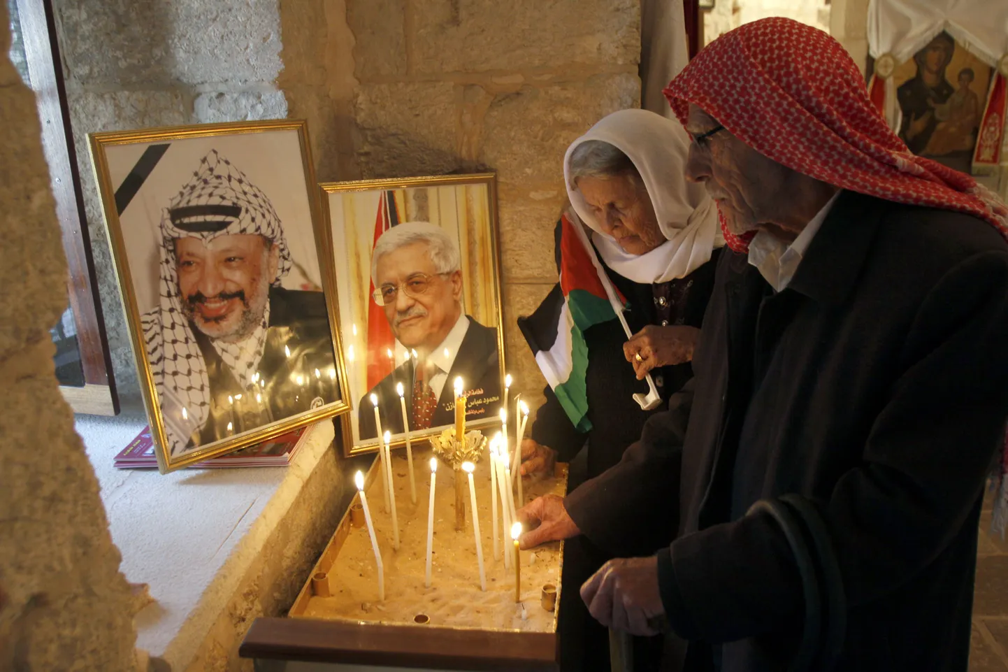 Palestiina kristlased panevad küünlaid PVO kunagise liidri Yasser Arafati (vasakul) ja Palestiina presidendi Mahmoud Abbasi fotode juurde.