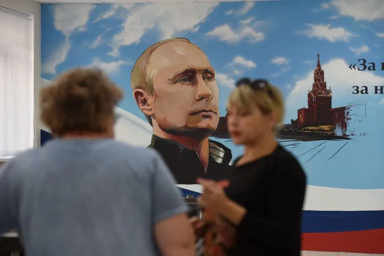 Люди на фоне плаката с изображением Путина.