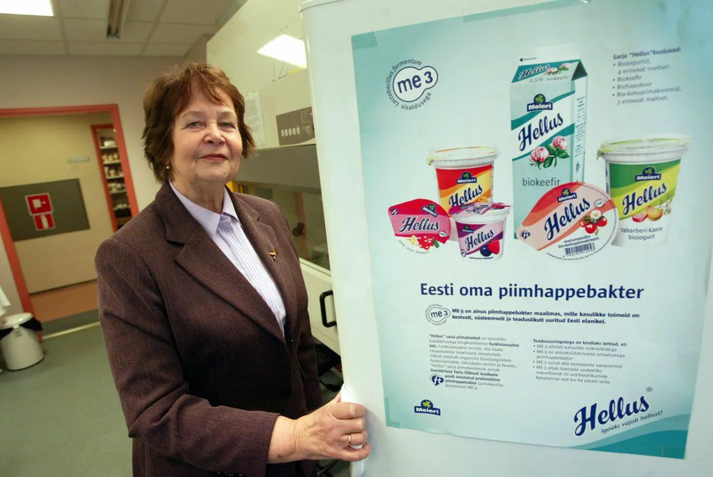 Marika Mikelsaar Dr. Helluse tootesarja tutvustava plakatiga. Sarja toodetes kasutatakse Mikelsaare juhitud töörühma poolt välja töötatud probiootilist bakterit ME-3..