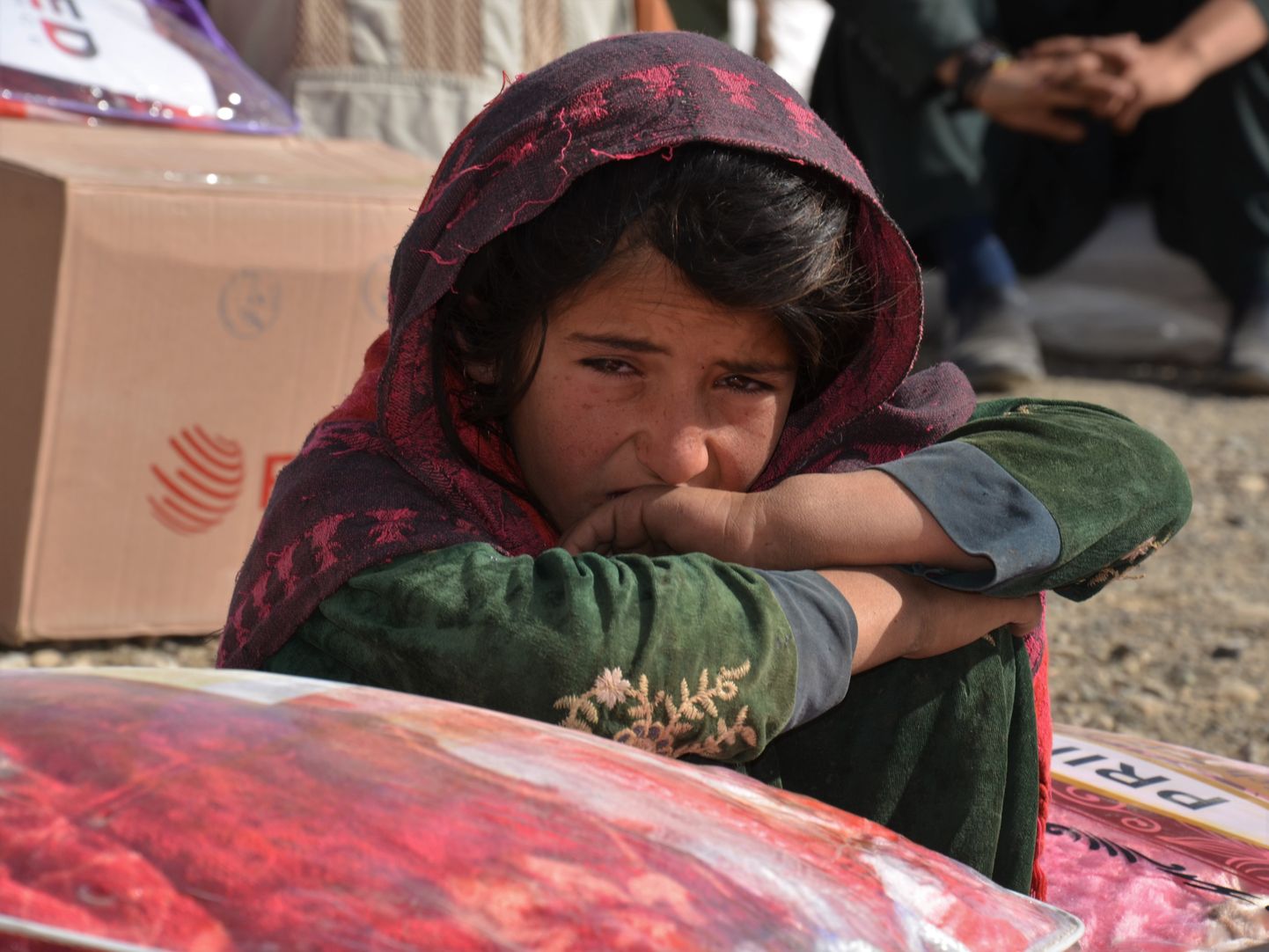 Afganistani tüdruk istumas humanitaarabi saadetise kõrval.