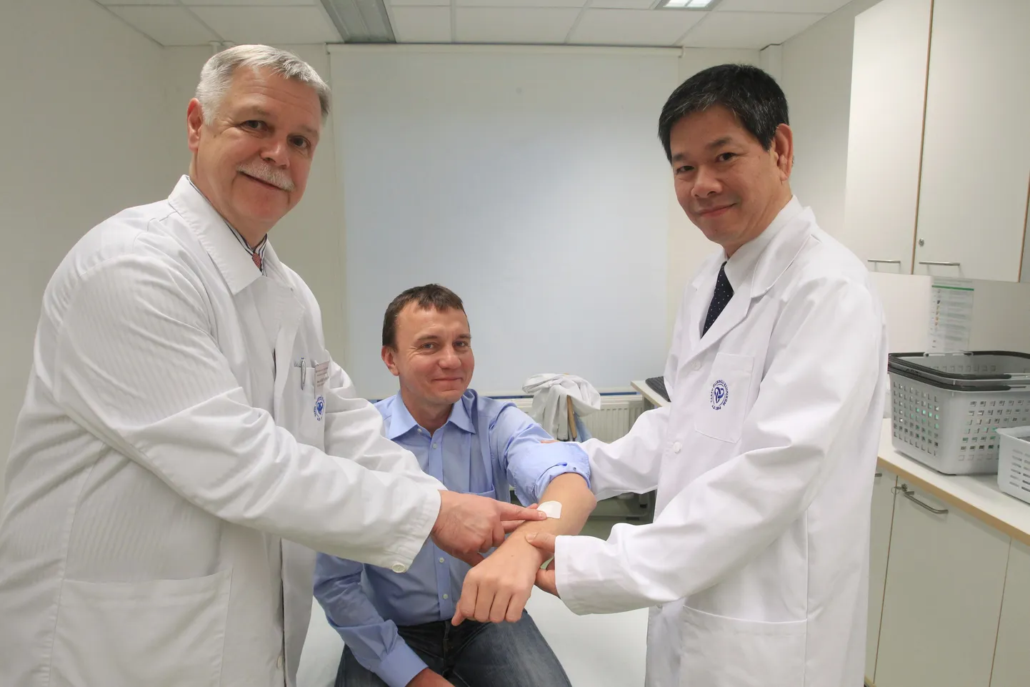 Tartu Ülikooli kliinikumi traumatoloogia ja ortopeedia kliiniku juhataja Aare Märtson (vasakul) ja Vietnamist pärit doktorant Ho Duy Binh on foto tegemiseks patsienti mängima pannud Tartu Ülikooli patofüsioloogia professori Sulev Kõksi.